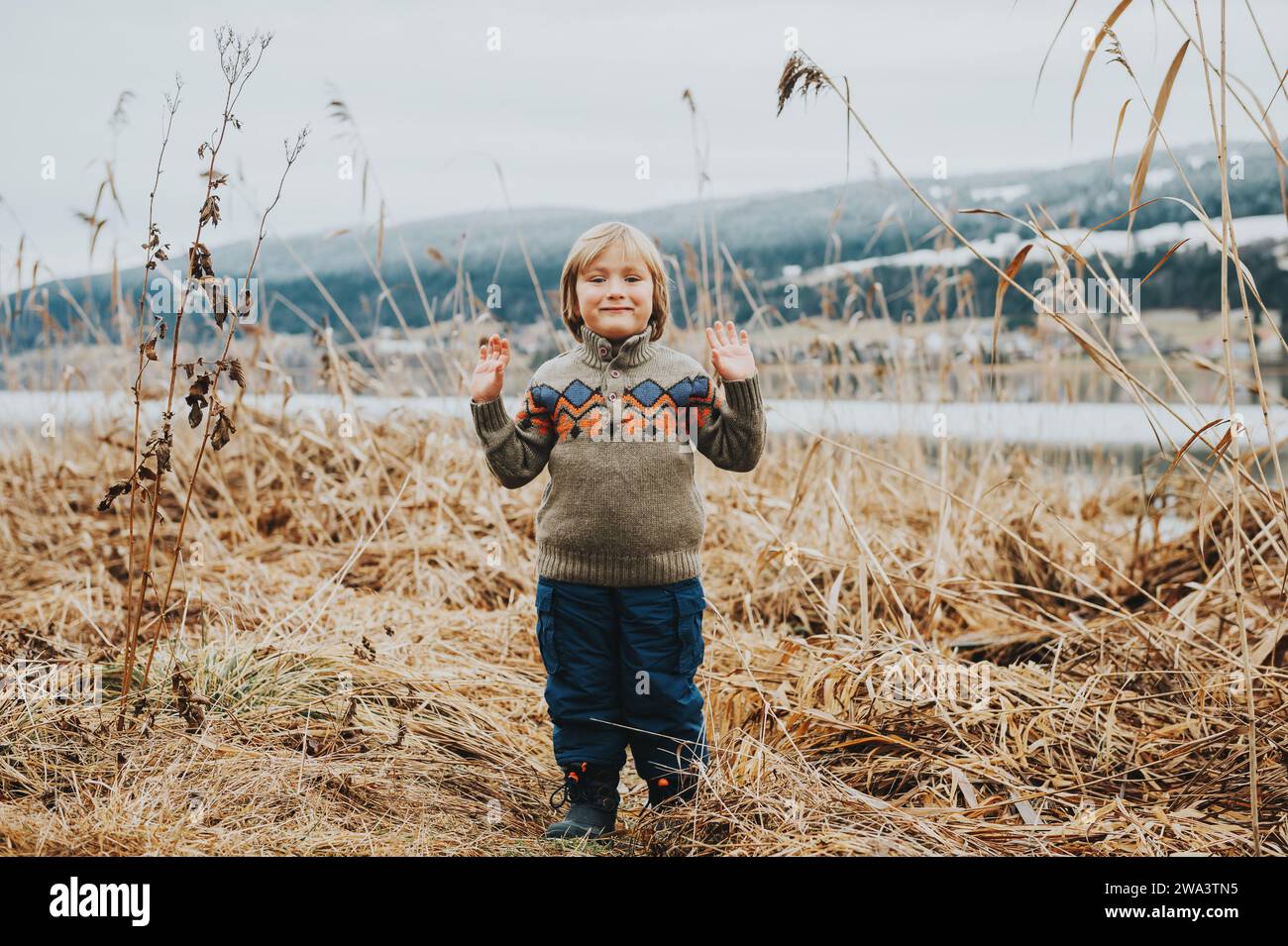 Außenporträt eines süßen kleinen Jungen von 4-5 Jahren, der an einem kalten Tag am See spielt Stockfoto