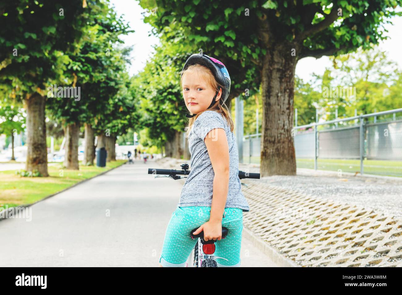 Kleines Mädchen, das im Park auf dem Fahrrad sitzt und über die Schulter blickt Stockfoto