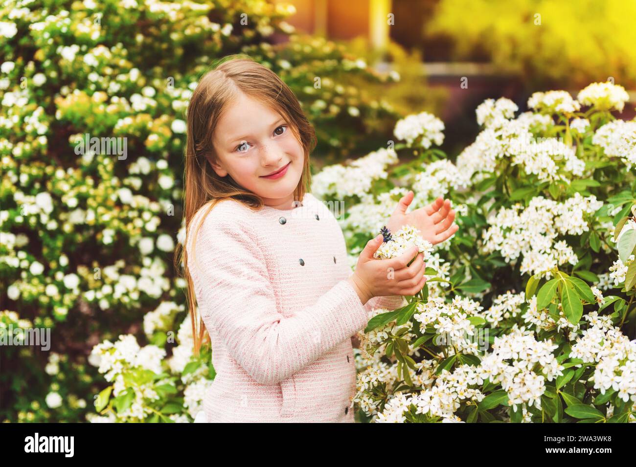Außenporträt eines 7-8-jährigen hübschen Mädchens mit Frühlingsblumen, in rosa Jacke Stockfoto