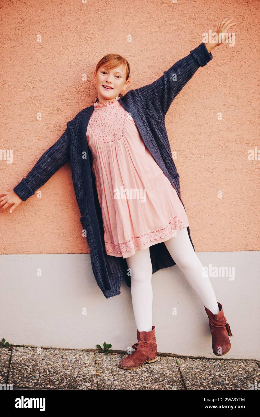 Außenporträt eines entzückenden jungen Mädchens mit weichem rosa Kleid, Kindermodell posiert vor beigefarbenem Wandhintergrund. Mode für junge Teenager Stockfoto