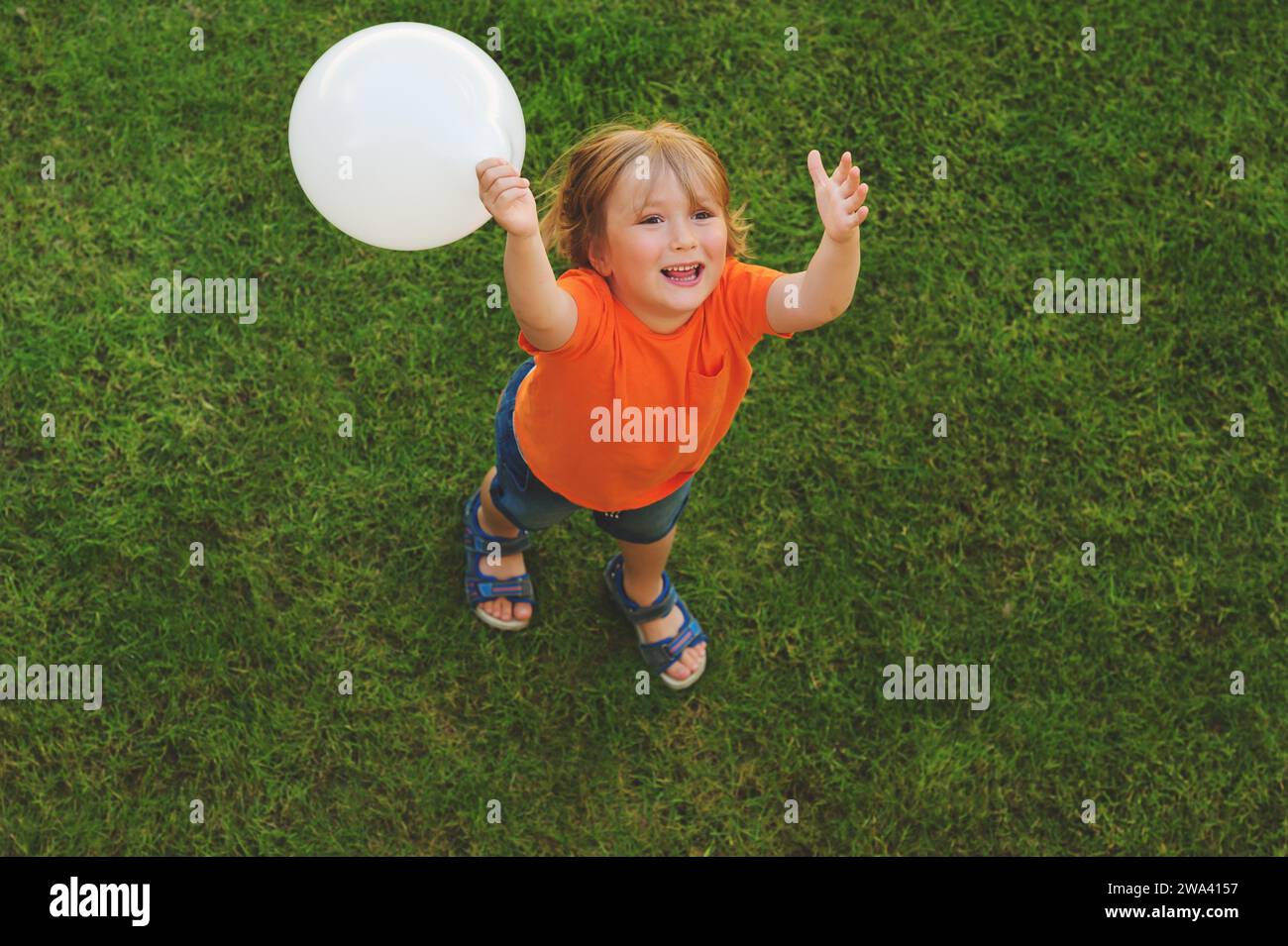 Glücklicher kleiner Junge von 4-5 Jahren, der draußen mit weißem Ballon spielt, Blick von oben Stockfoto