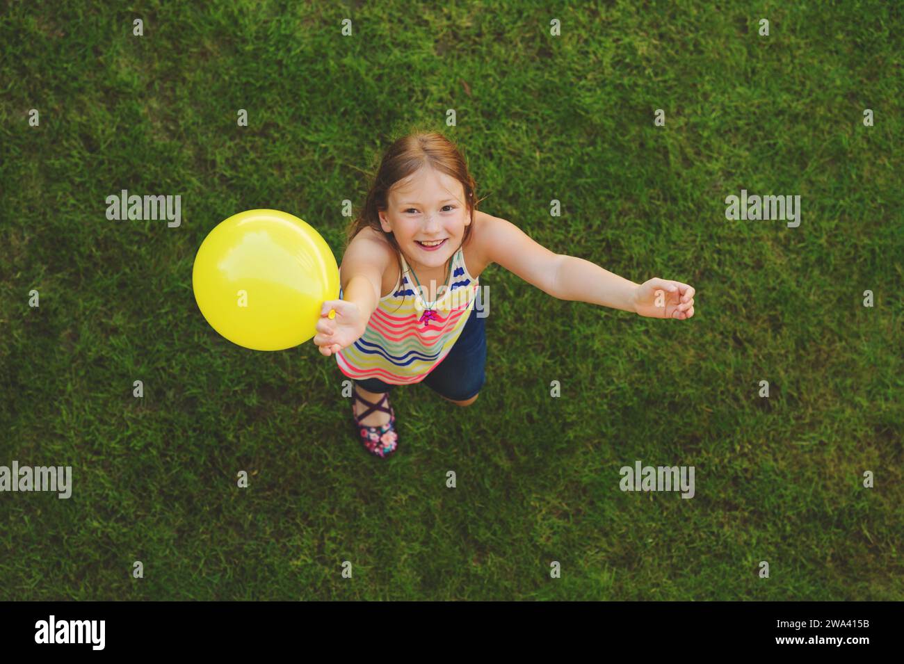 Glückliches, kleines Mädchen von 8-9 Jahren, das draußen mit weißem Ballon spielt, Blick von oben Stockfoto