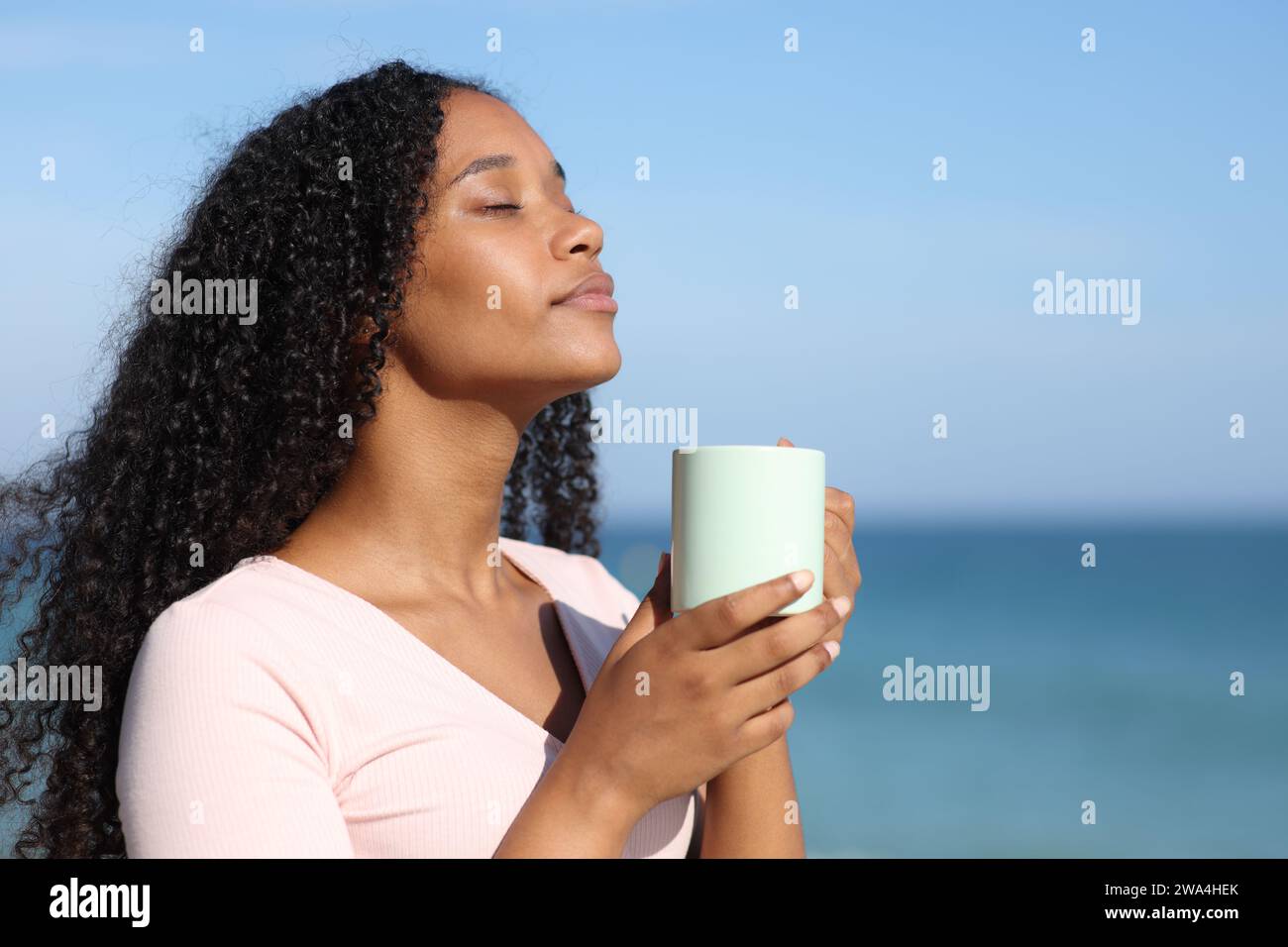 Eine ernste schwarze Frau riecht am Strand Kaffee Stockfoto