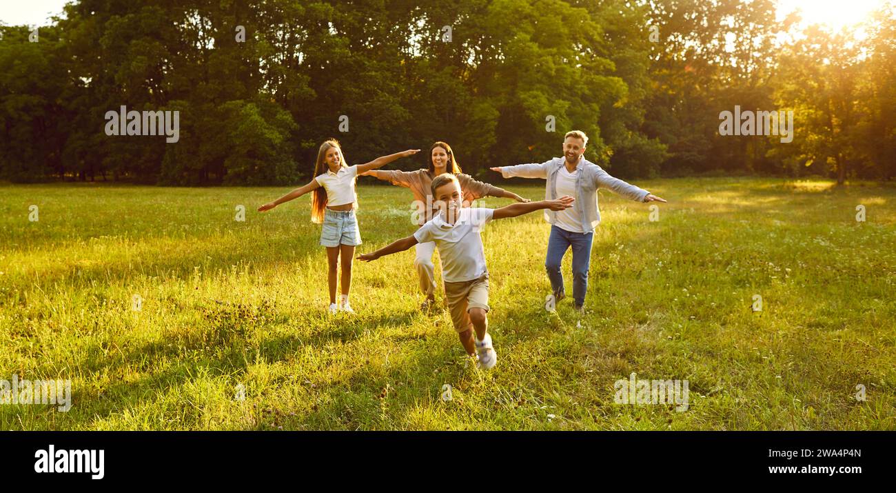 Glückliche Familie mit zwei Kindern, die laufen und Spaß im Sommerpark bei Sonnenuntergang haben. Stockfoto