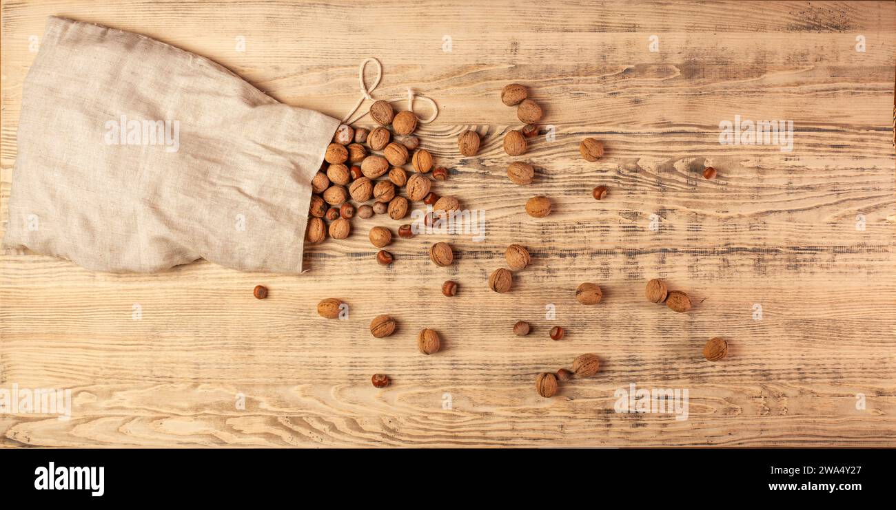 Große Tüte Sackleinen mit Walnüssen und Haselnüssen. Nüsse sind auf einem großen Holzbrett verstreut. Hölzerner Hintergrund. Draufsicht. Stockfoto