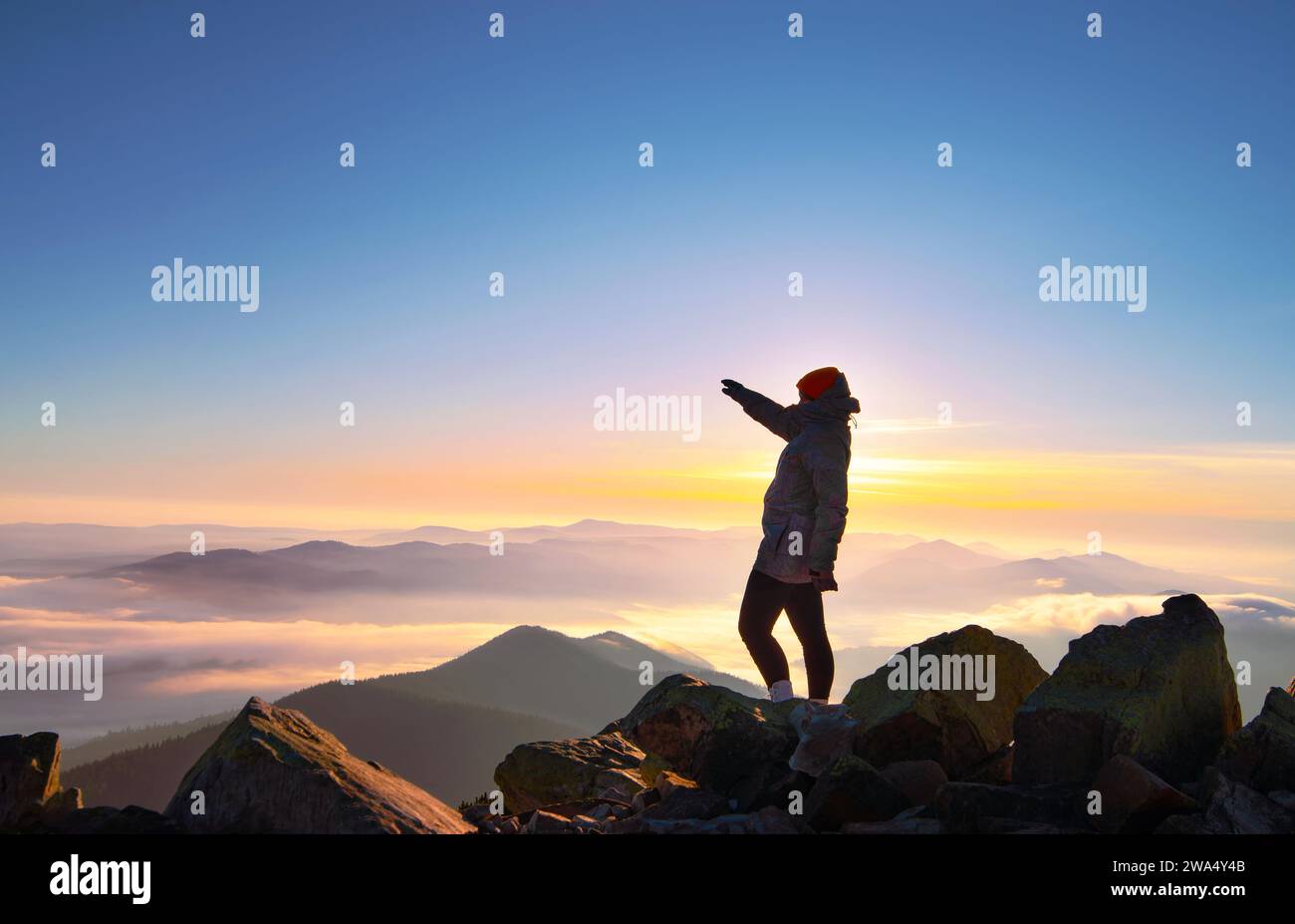 Mädchen mit erhobener Hand auf dem Berggipfel bei schönem Morgensonnenaufgang. Stockfoto