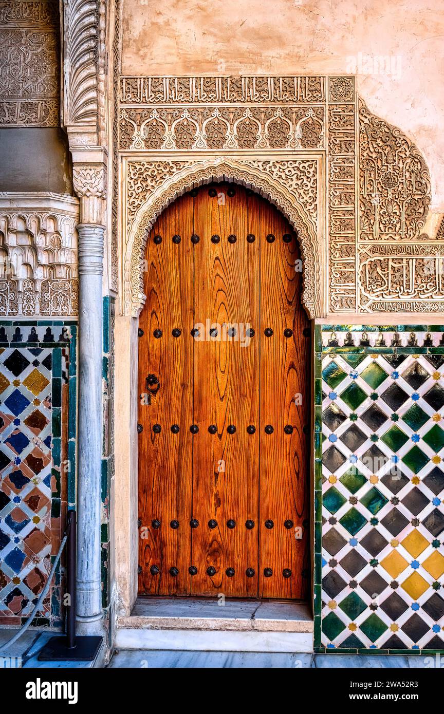 Holztür in einer Wand mit Fliesen und Steinschnitzereien in der Alhambra, Spanien. Der mittelalterliche Ort gehört zum UNESCO-Weltkulturerbe Stockfoto