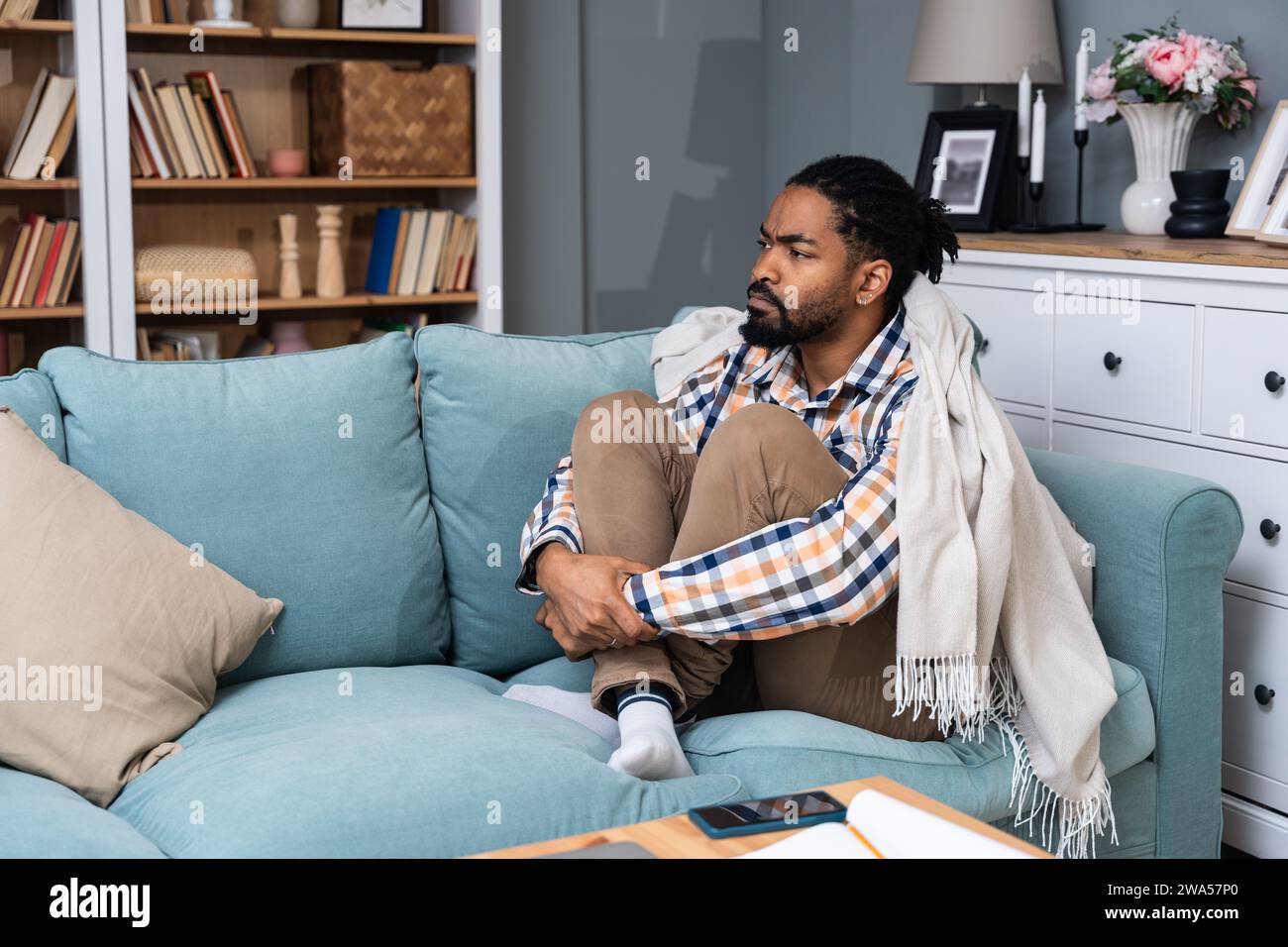Junger deprimierter Afroamerikaner, der mit gekreuzten Armen auf dem Sofa sitzt. Rassismus-Opfer für Hautfarbe schwarz männlich mit Depressionen nach dem sein Stockfoto