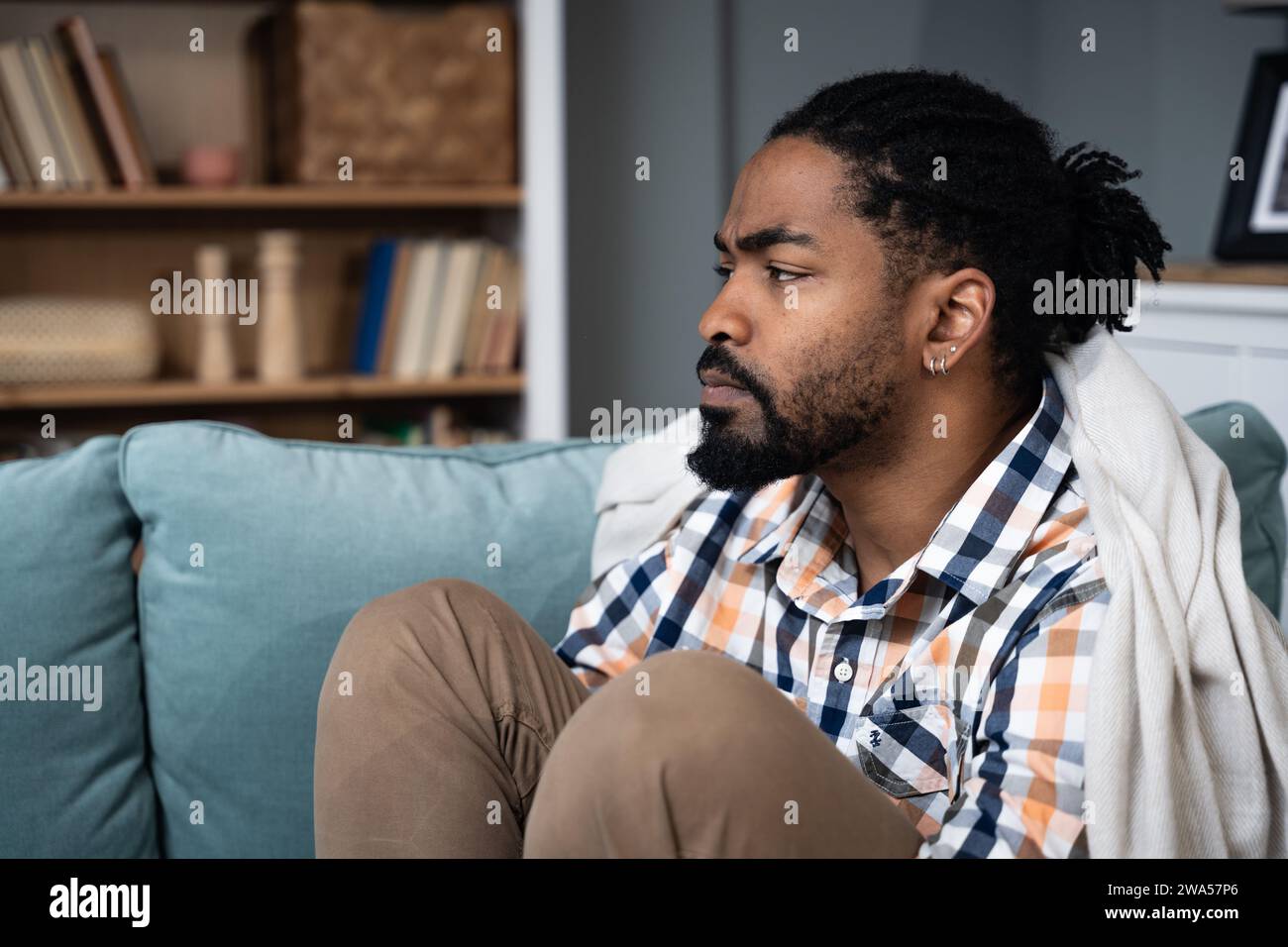Junger deprimierter Afroamerikaner, der mit gekreuzten Armen auf dem Sofa sitzt. Rassismus-Opfer für Hautfarbe schwarz männlich mit Depressionen nach dem sein Stockfoto