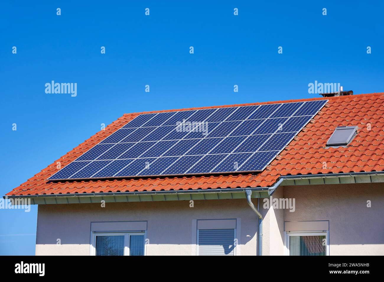 Solarzellen auf einem roten Dach vor blauem Himmel Stockfoto