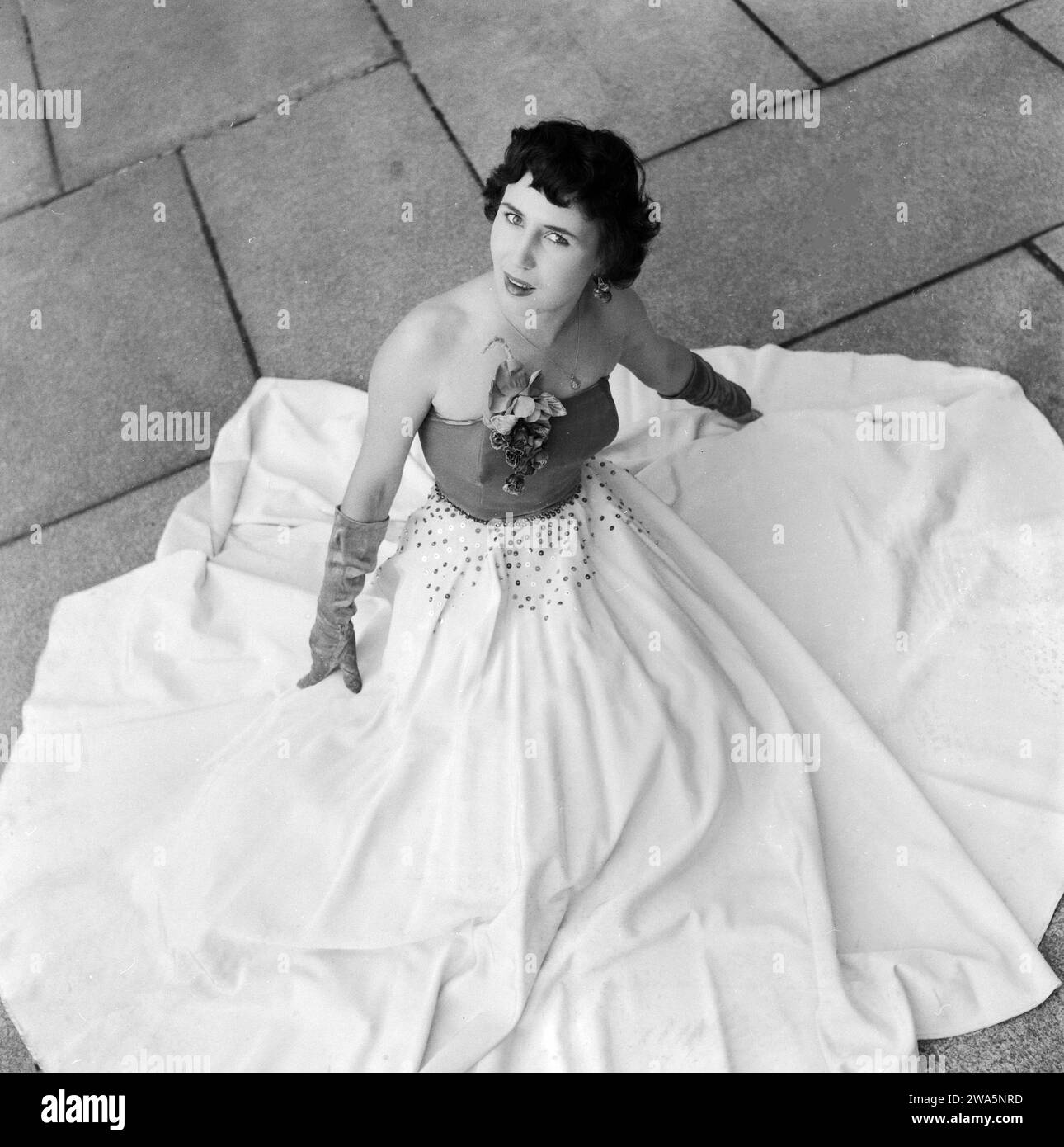 Eine junge Frau präsentiert auf dem Boden sitzend ein weißes Abendkleid mit ausgebreitetem Rock, Deutschland Mitte 1950er Jahre. Stockfoto