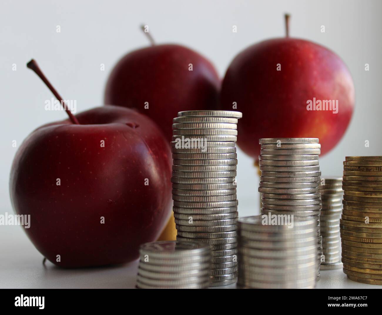 Verschwommene rote Äpfel hinter den Münzstapeln, isoliert auf weiß. Konzeptfoto zur Veranschaulichung des steigenden Obstpreises Stockfoto