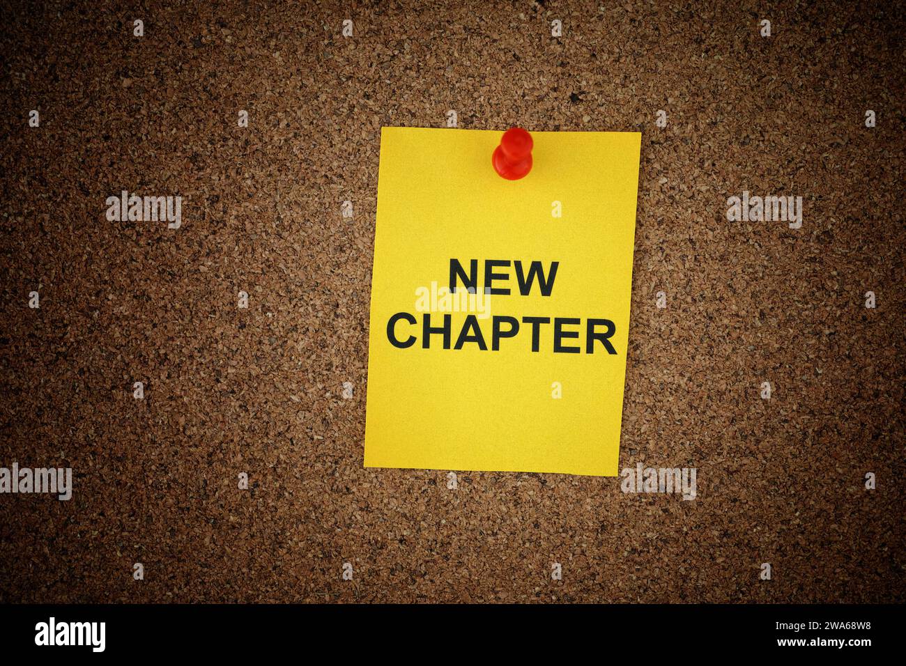 Eine gelbe Notiz aus Papier mit den Worten Neues Kapitel drauf, an ein Korkbrett geheftet. Nahaufnahme. Stockfoto