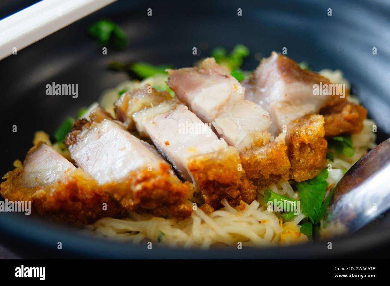 Eine Schüssel Eiernudeln serviert mit knusprigem Bauchschwein darauf. In Thailand gehören Nudeln und knuspriges Bauchschwein zu den beliebtesten Gerichten. Stockfoto