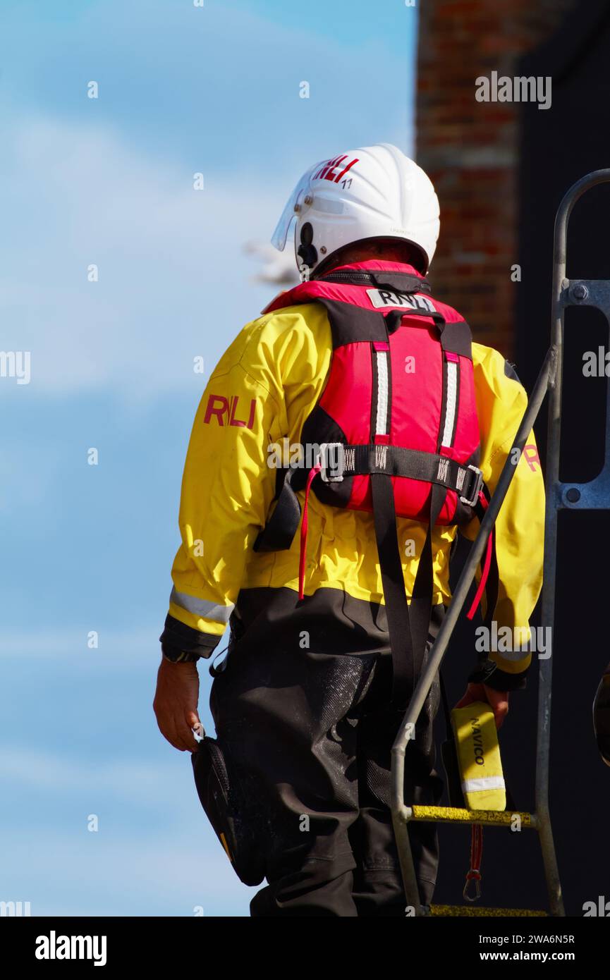 RNLI Lifeboat Crew Member in gelbem Trockenanzug, Schutzhelm und Schwimmweste, die sich auf den Weg zur See an der Mudeford Lifeboat Station vorbereiten Stockfoto