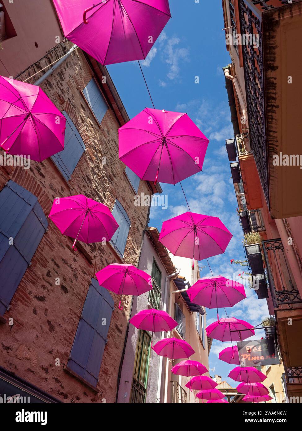 Eine enge Straße in Cadaqués Spanien, die mit pinkfarbenen Sonnenschirmen dekoriert ist Stockfoto