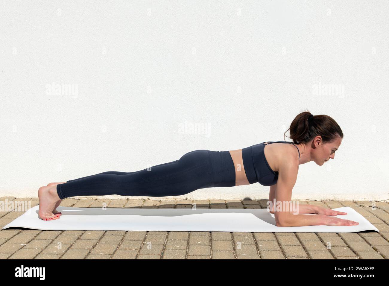 Frau in Sportbekleidung, die im Freien auf einer Fitnessmatte trainiert. Plank Pose. Stockfoto