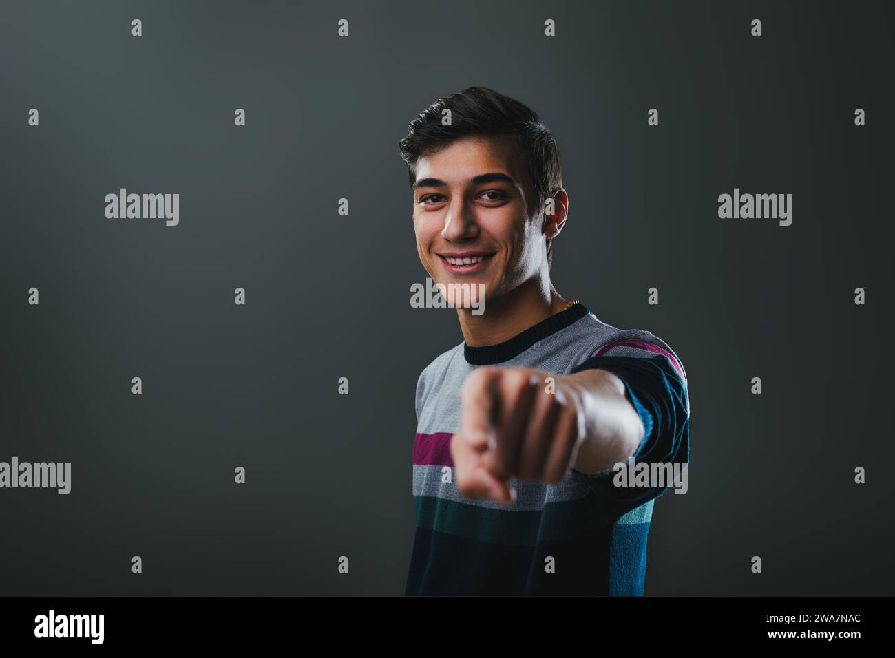 Eine junge Figur mit einem lebhaften Lächeln streckt eine einladende Hand in einem coolen gestreiften Pullover aus Stockfoto