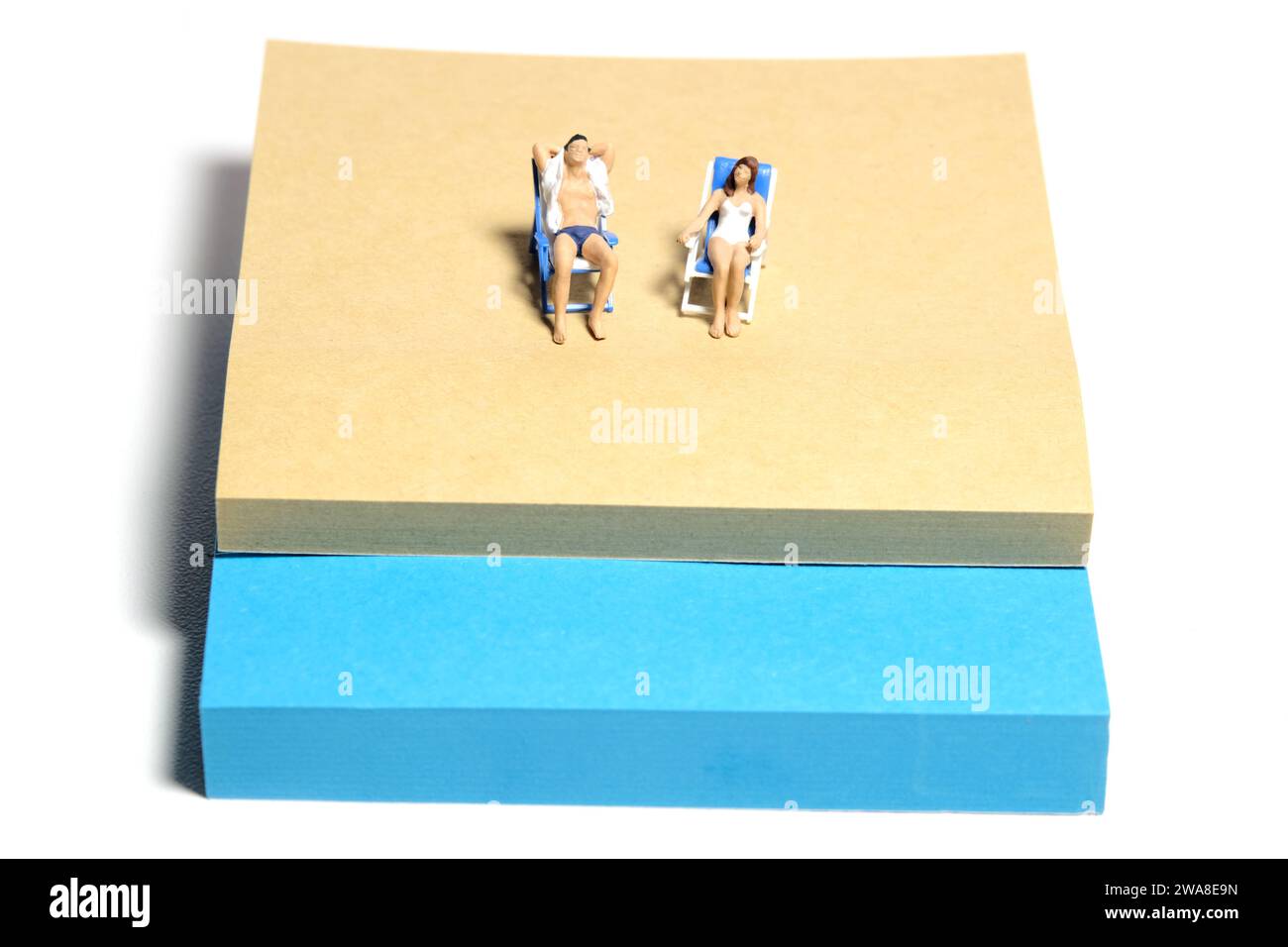 Kreative Miniaturmenschen spielzeugfiguren fotografieren. Installation von Haftnotizen. Ein Paar, das auf der Strandbank am Strand relaxt. Isoliert auf weißer Rückseite Stockfoto