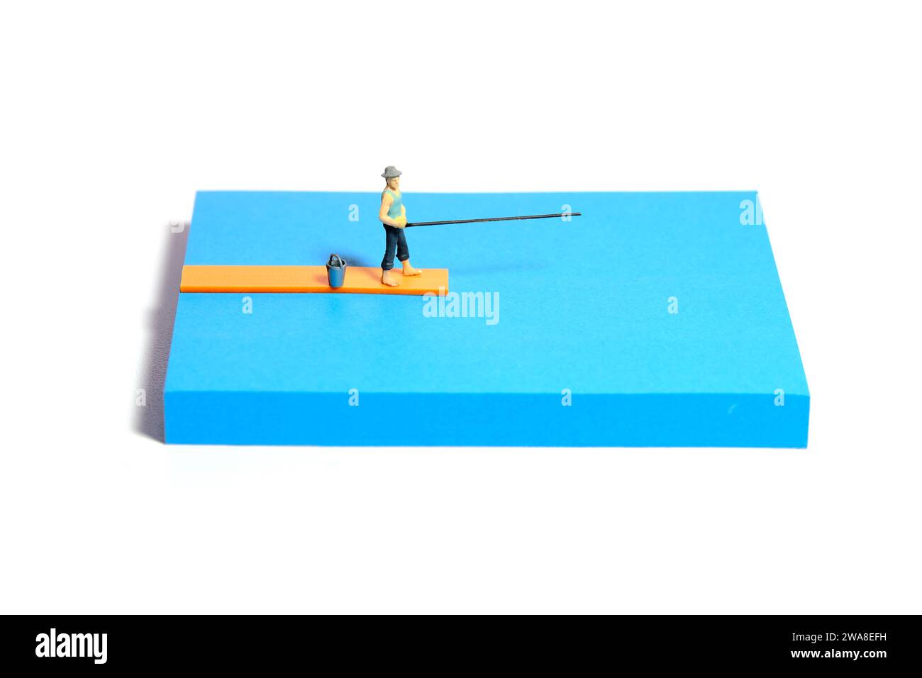 Kreative Miniaturmenschen spielzeugfiguren fotografieren. Installation von Haftnotizen. Ein Mann, der über einer Holzbrücke am Fluss, See oder Strand fischt. Isoliert auf W Stockfoto