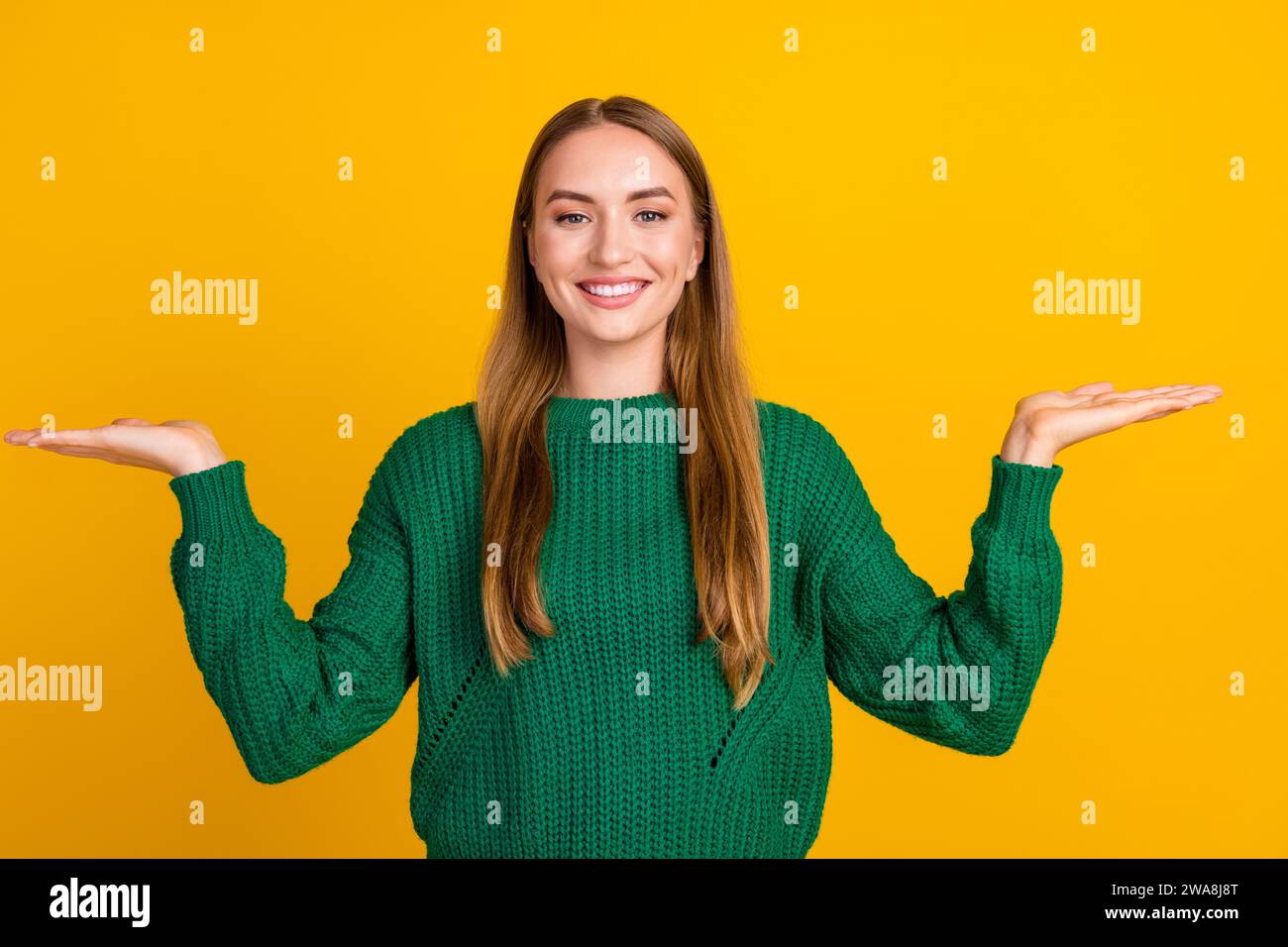 Portraitfoto eines optimistischen jungen lächelnden Mädchens, das einen grünen Pullover trägt, der zwei Palmen mit gleichem Gewicht auf gelbem Hintergrund hält Stockfoto