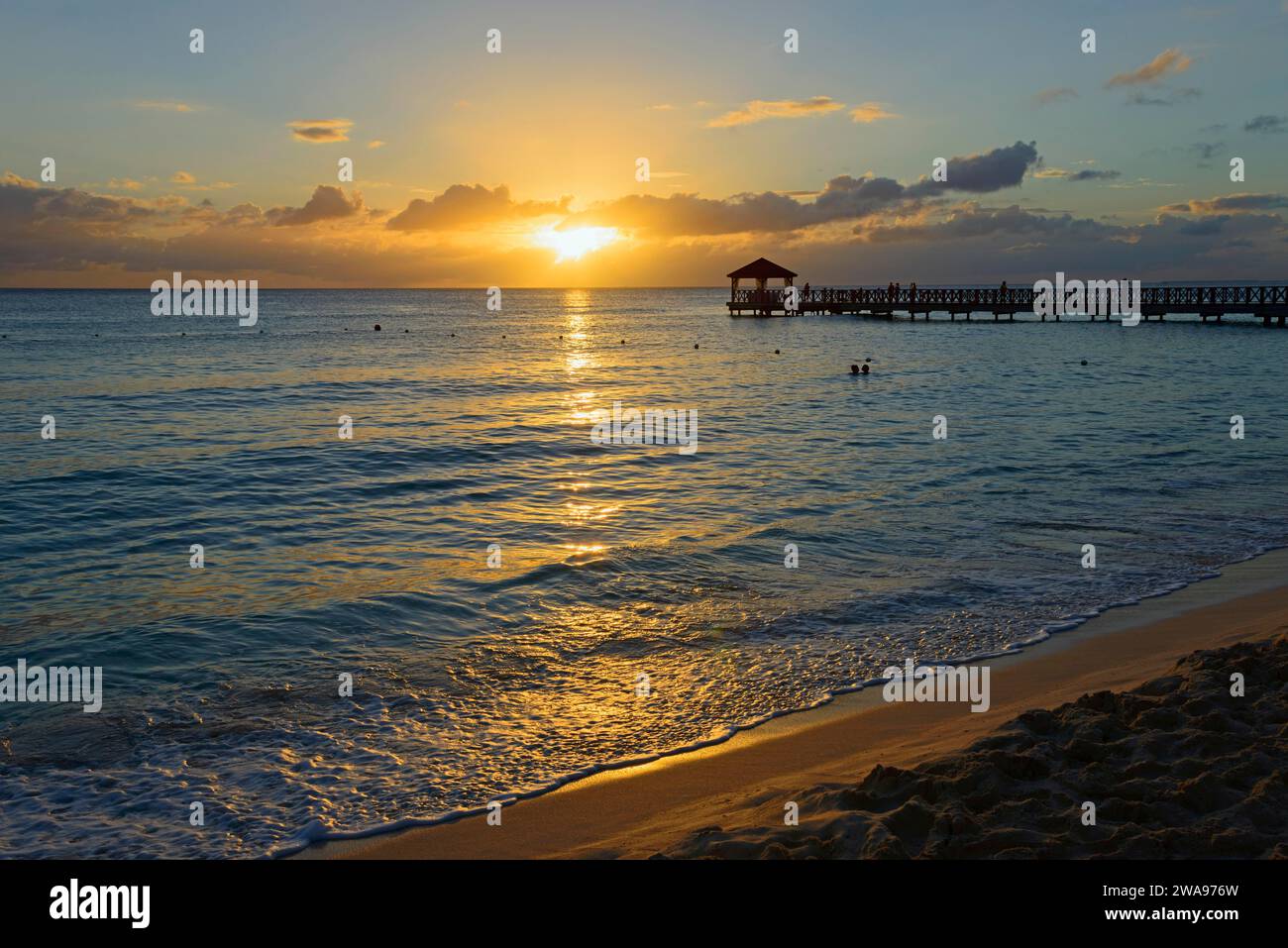 Ein friedlicher Sonnenuntergang am Strand mit Blick auf einen Steg und das reflektierende Meer Stockfoto