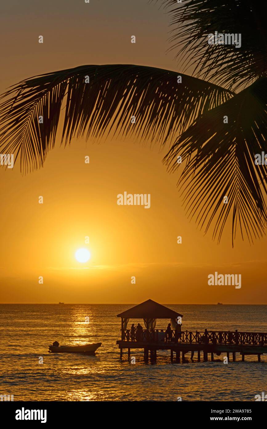 Beruhigende Szene eines Sonnenuntergangs hinter einem Pier, eingerahmt von Palmblättern Stockfoto