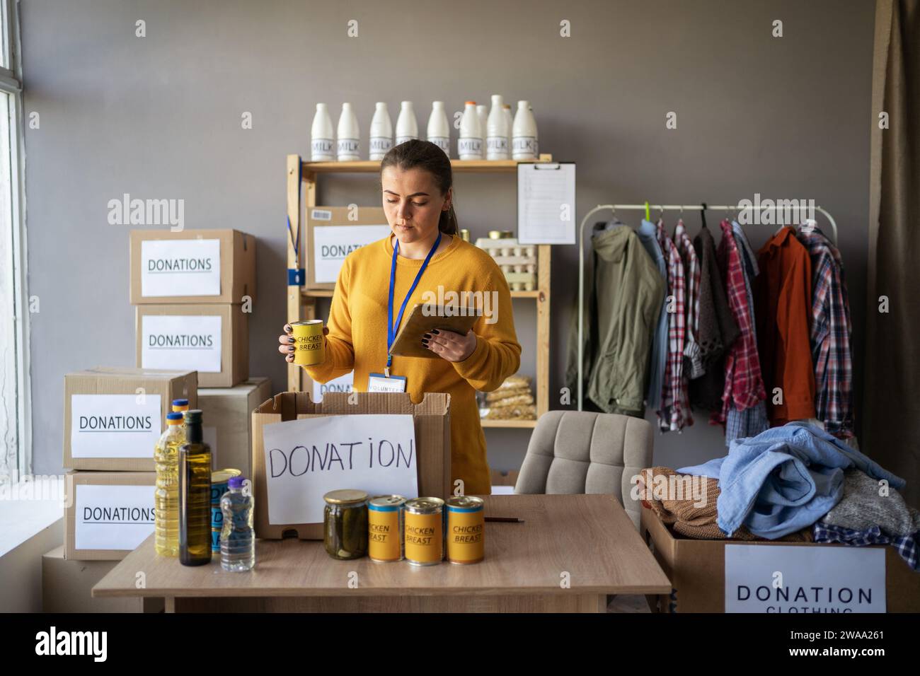 Happy smiling female volunteer with digital tablet packaging food in box working at humanitarian aid or refugee assistance center. charity, donation Stockfoto