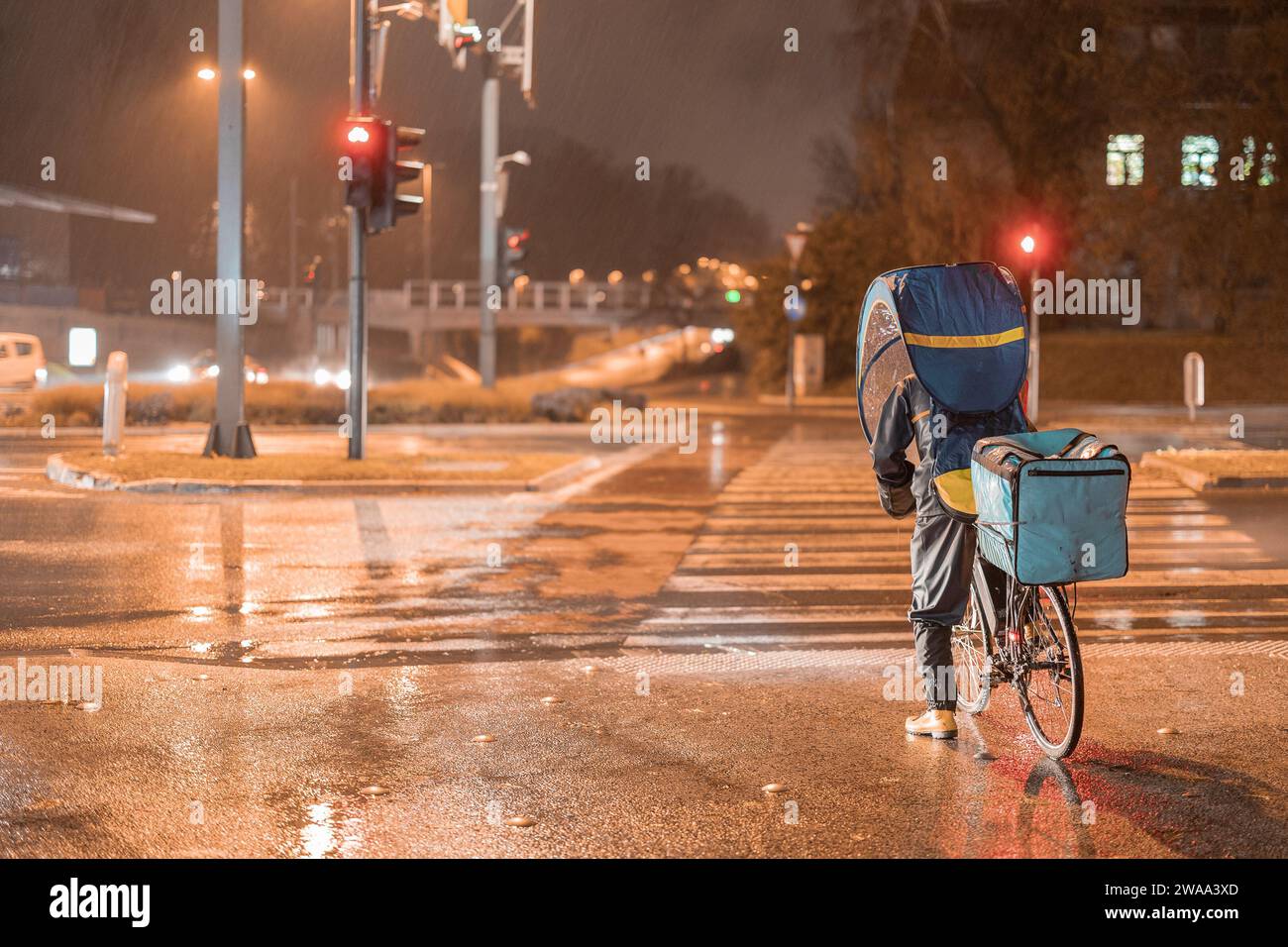 Lebensmittelzustellung Radfahrer bei Nacht und Regen liefern Waren, während sie mit einem mobilen Regenschirm oder einer wetterfesten Schutzabdeckung geschützt sind. Auf einem stehen Stockfoto