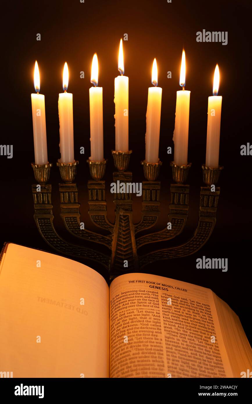 Die Heilige Bibel ist offen für das Buch Genesis in Kapitel 1 und Menora mit 7 Kerzen isoliert auf dunklem Hintergrund. Stockfoto