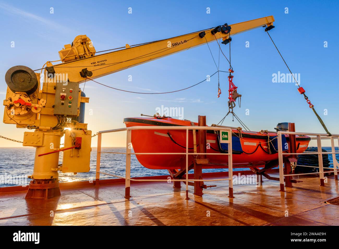 Orangefarbenes Rettungsboot auf großem Frachtschiff und Kran. Man-über-Bord-Übung. Rettungsboottraining. Stockfoto