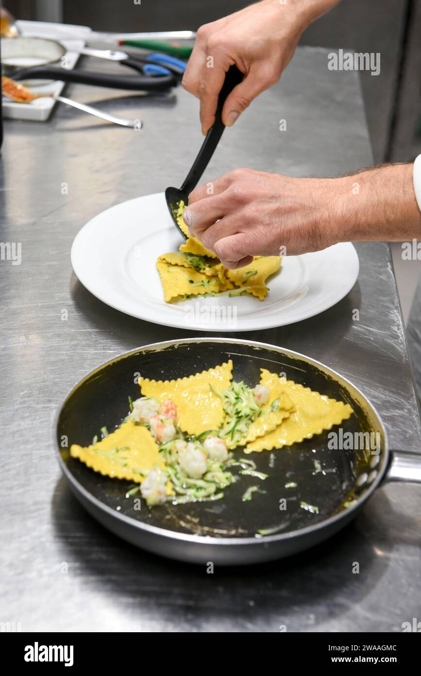 Hoher Winkel eines anonymen Mannes, der köstliche Ravioli-Pasta mit Gurke und Garnelen auf den Teller legt, während er in der Restaurantküche arbeitet Stockfoto