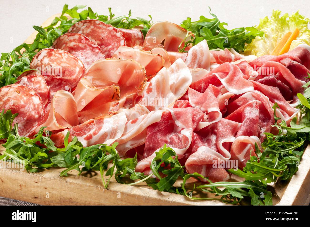Großer Winkel von verschiedenen frischen Salaten mit köstlichem gemischten italienischen Schinken und Salami auf Holztablett Stockfoto