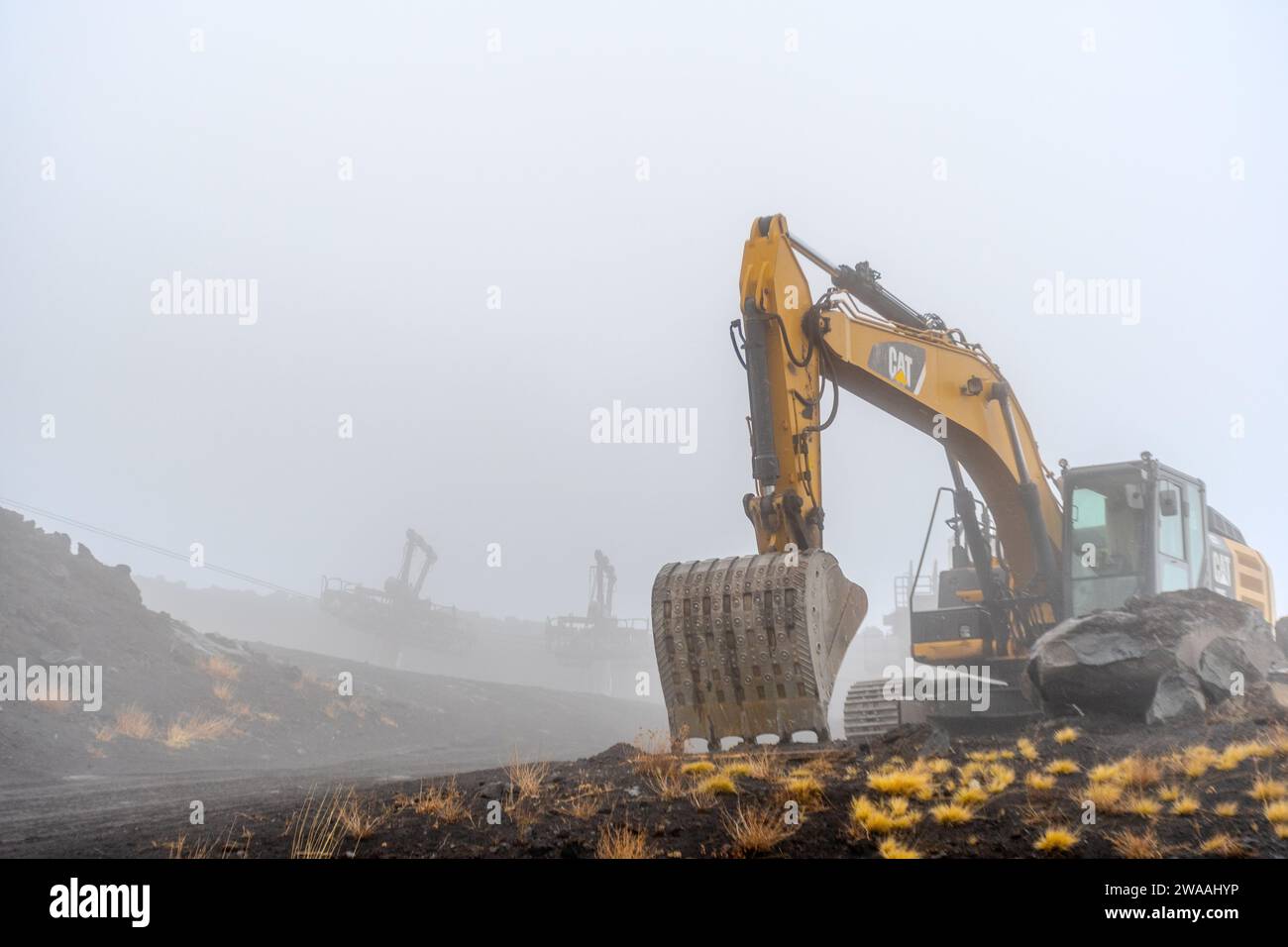 Bagger für Arbeiten in rauer Landschaft unter nebelhaltigen Bedingungen. Stockfoto