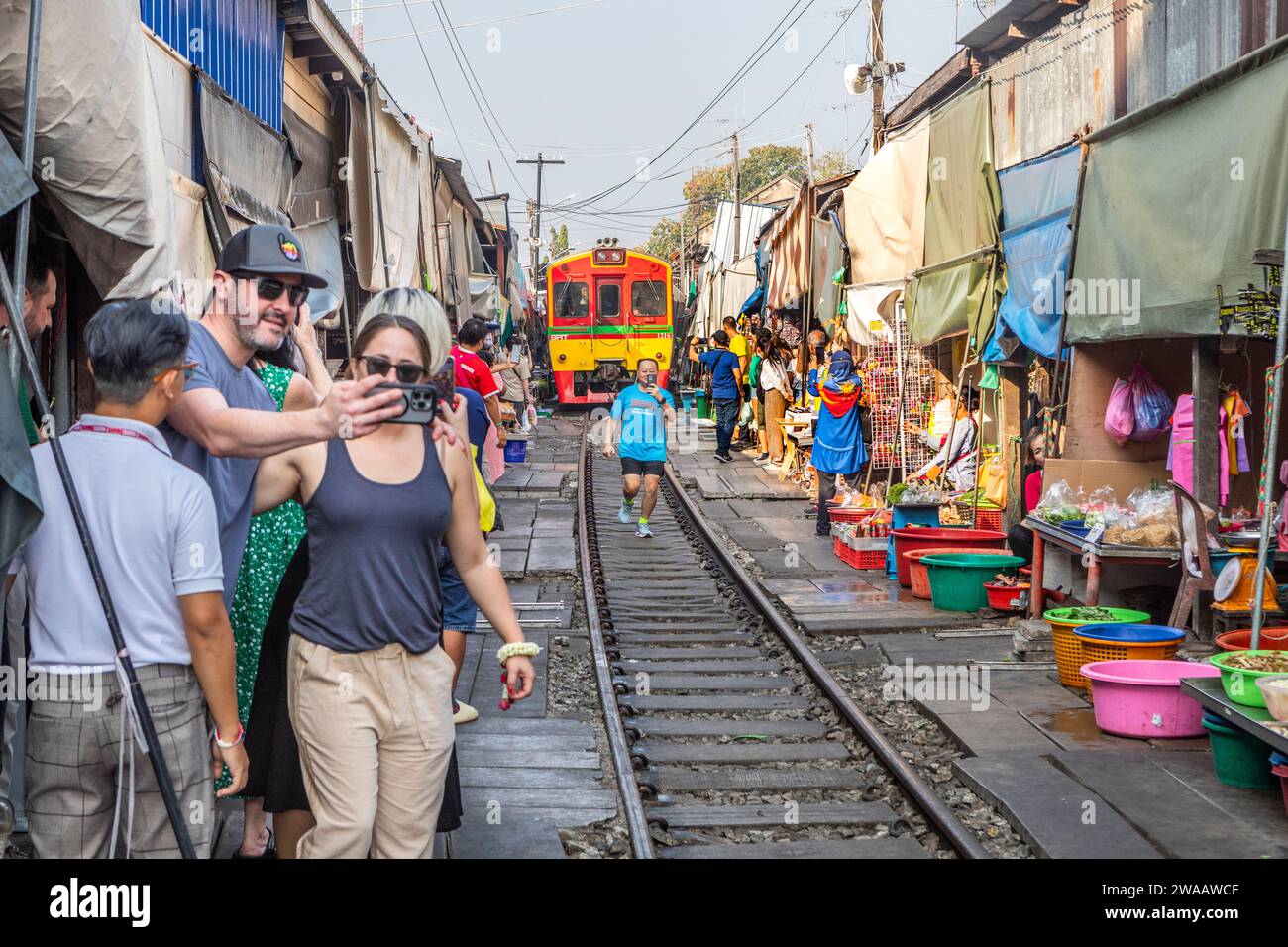Ein Zug fährt langsam durch den Mae Klong Railway Market in Thailand, während Touristen Selfies machen. Stockfoto