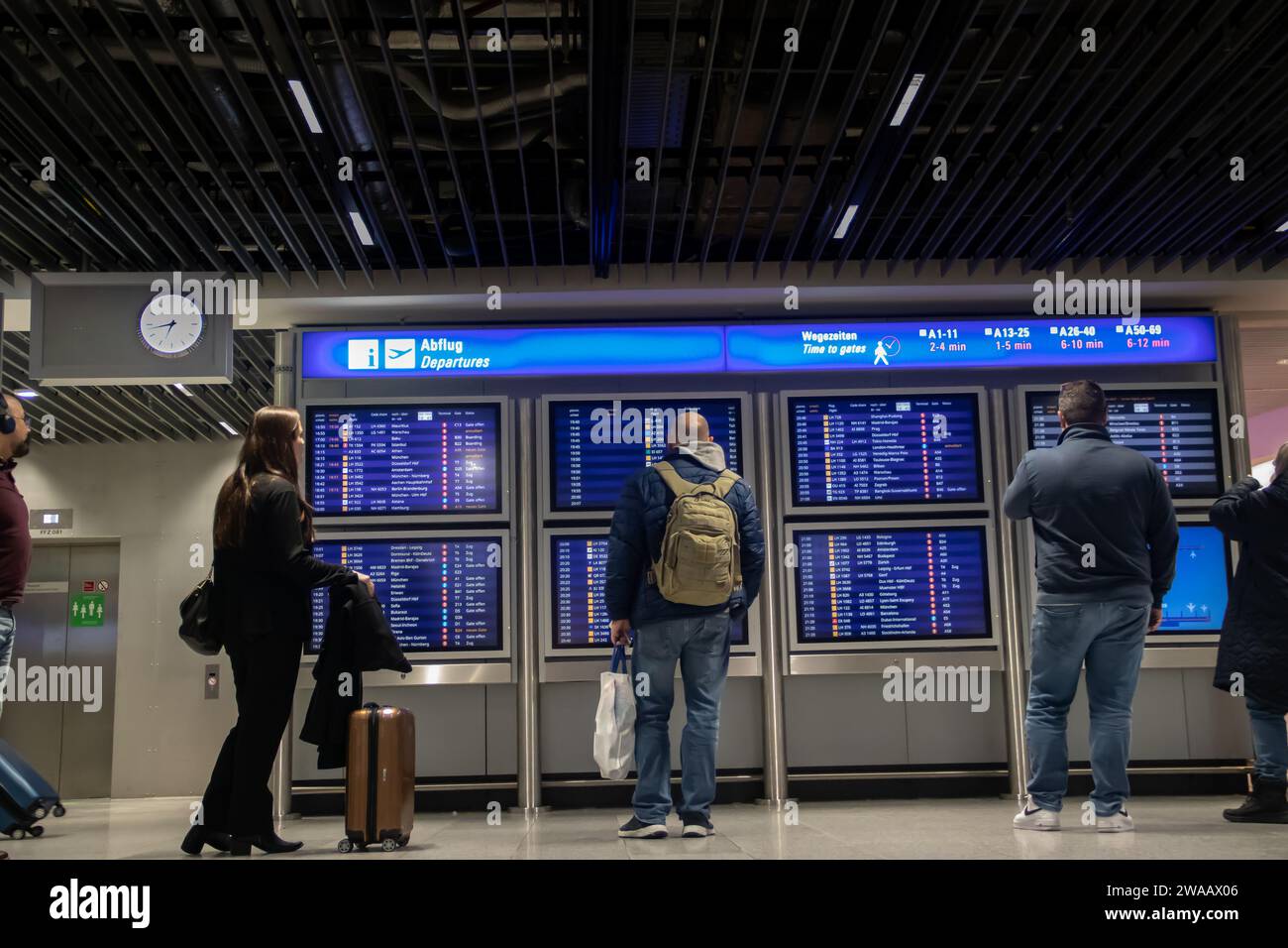 Nachts kam eine Menschenmenge vor der Informationstafel am Flughafen, die nach dem Einsteigen in die Transitzone nach Fluginformationen sucht Stockfoto