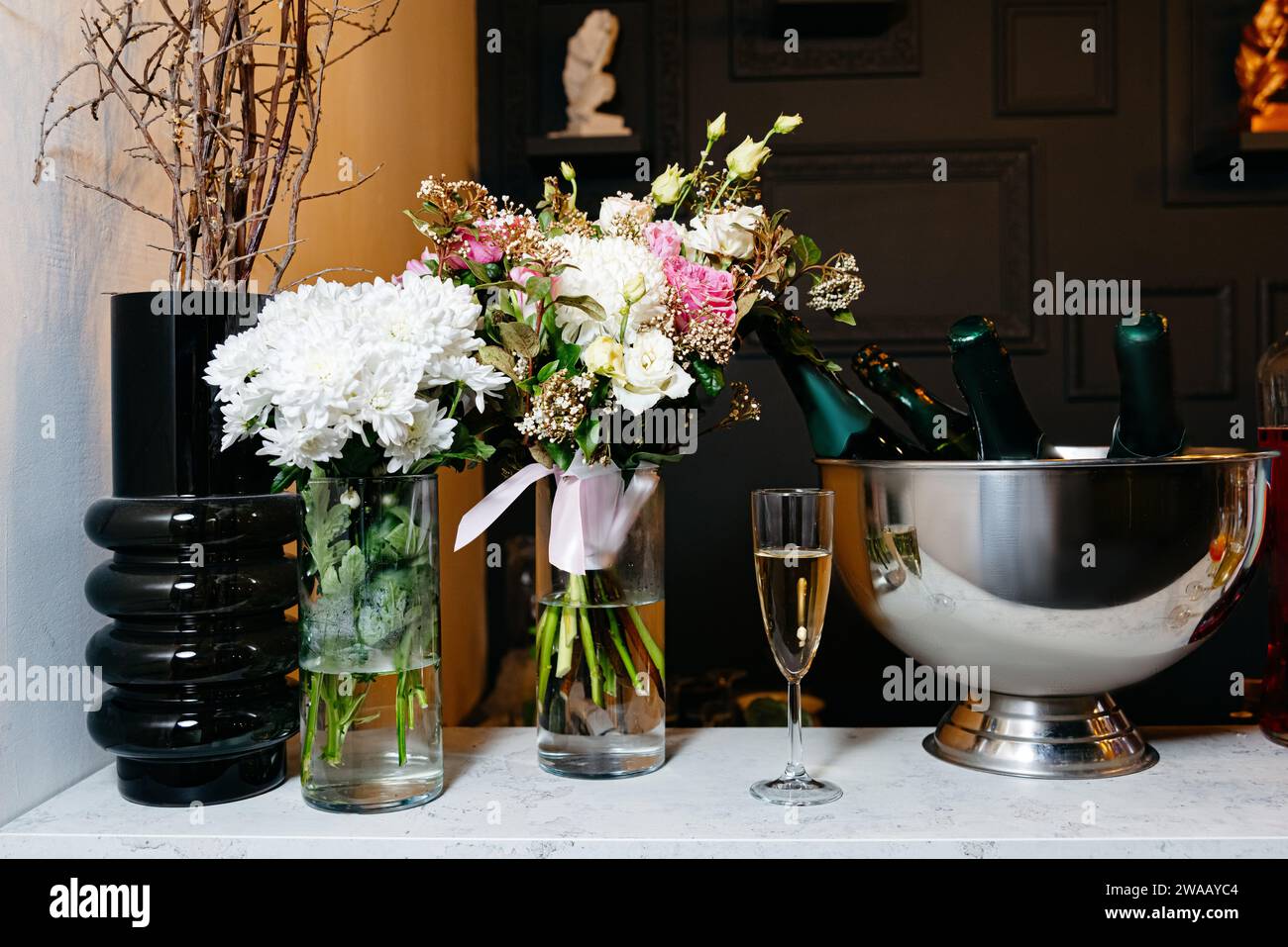 Elegante Veranstaltungseinrichtung mit wunderschönen Blumenarrangements in Vasen und gekühltem Champagner in einem silbernen Eiskübel für eine elegante Atmosphäre. Stockfoto