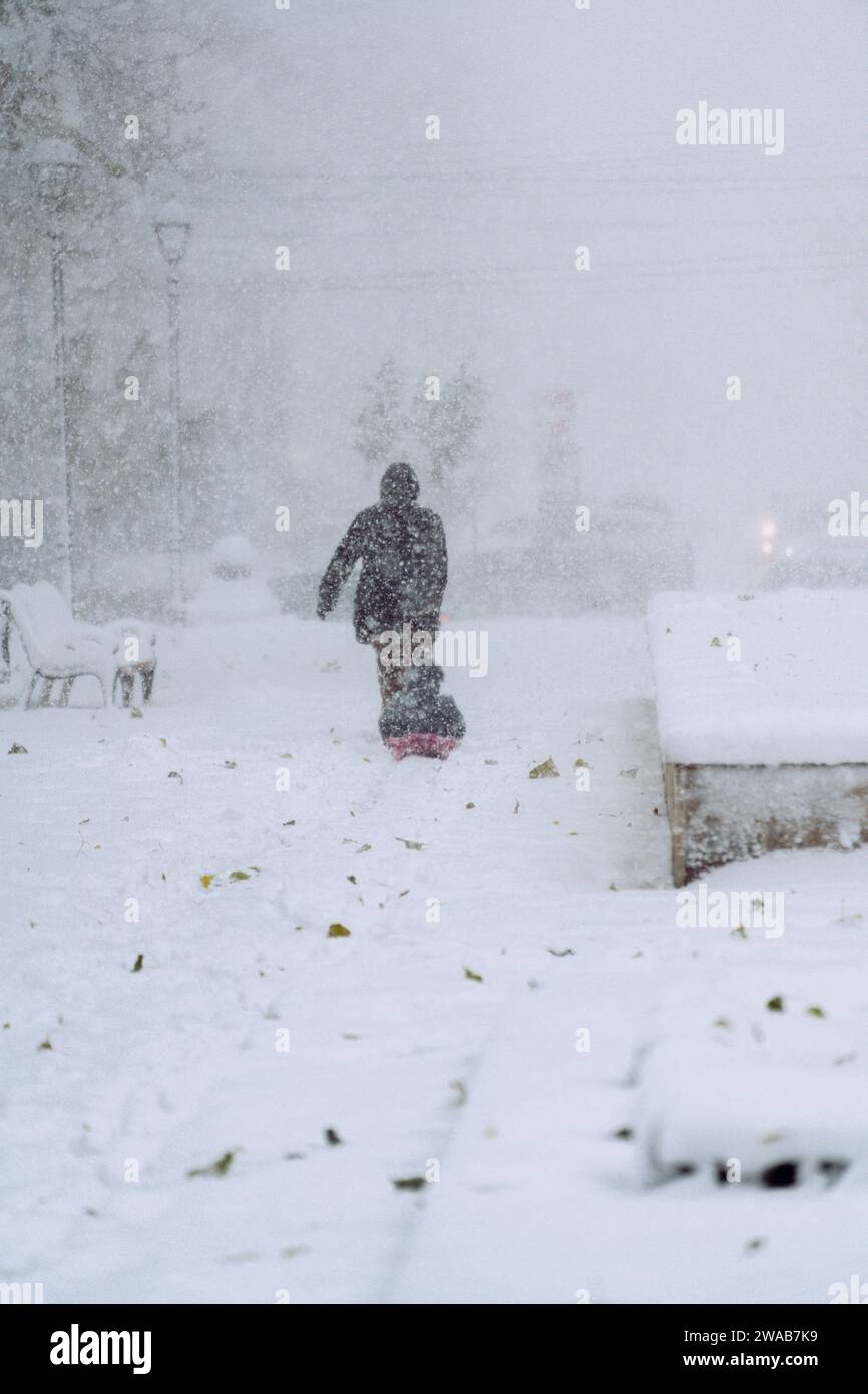 Frau zieht Kind auf einem Schlitten bei starkem Schneefall in der Stadt Stockfoto