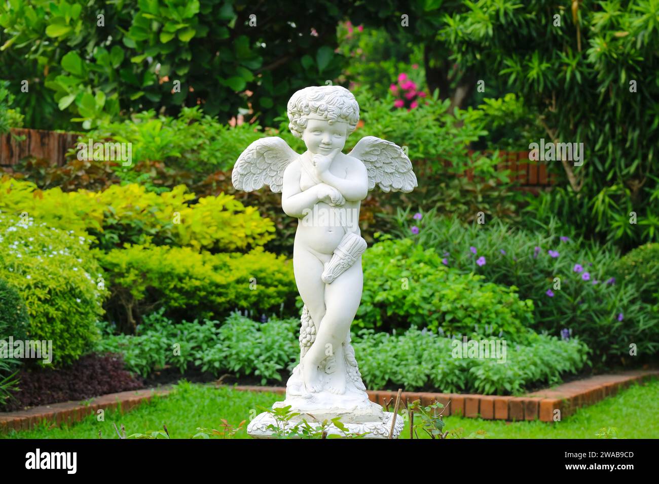 Entzückende freche Cupid-Skulptur in einem frisch grünen Garten Stockfoto