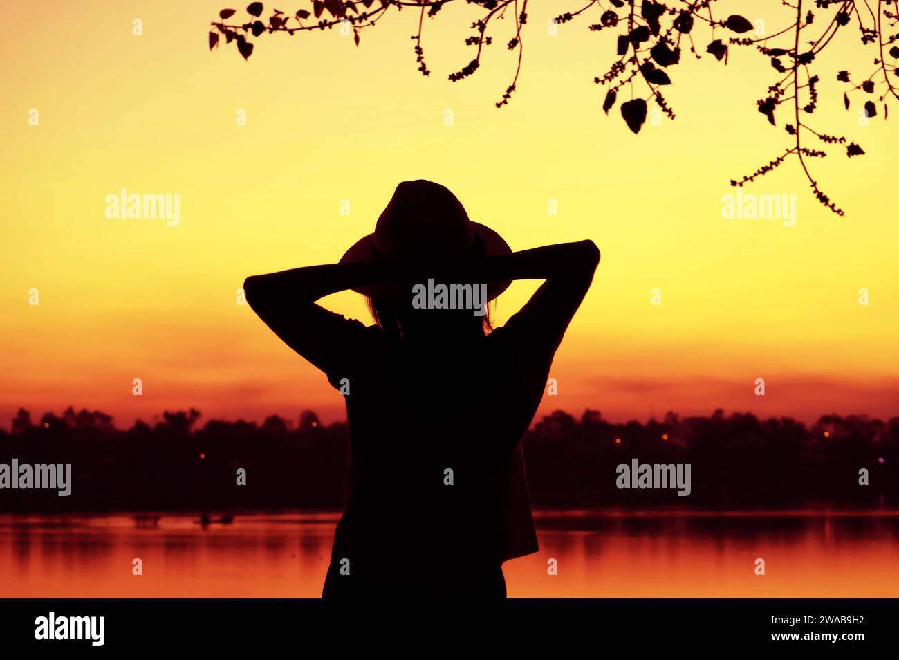 Silhouette einer Frau, die sich am Seeufer vor atemberaubendem, farbenfrohen Himmel entspannt Stockfoto