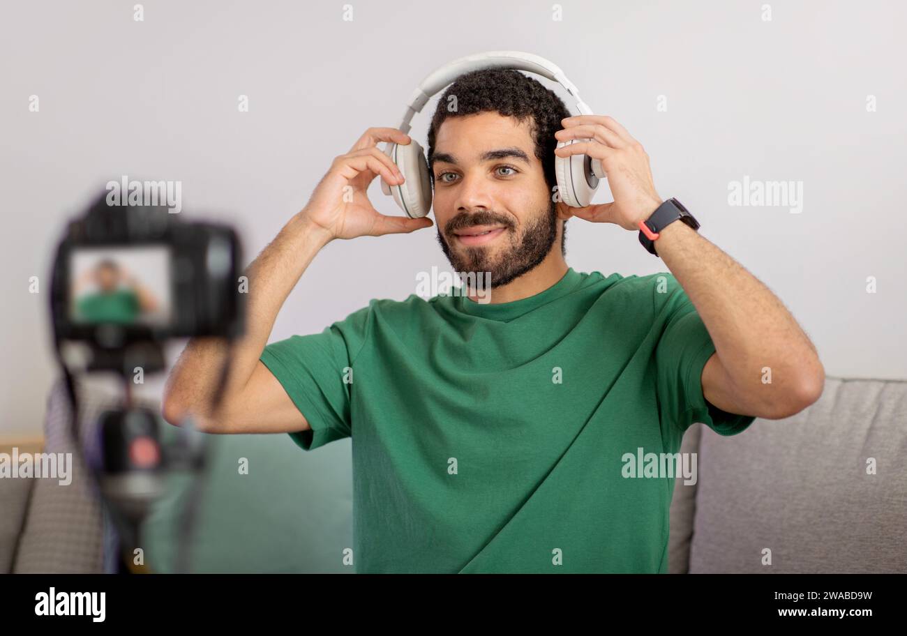 Content Creator in einem lässigen grünen T-Shirt genießt Musik auf weißen Kopfhörern und lächelt in die Kamera Stockfoto