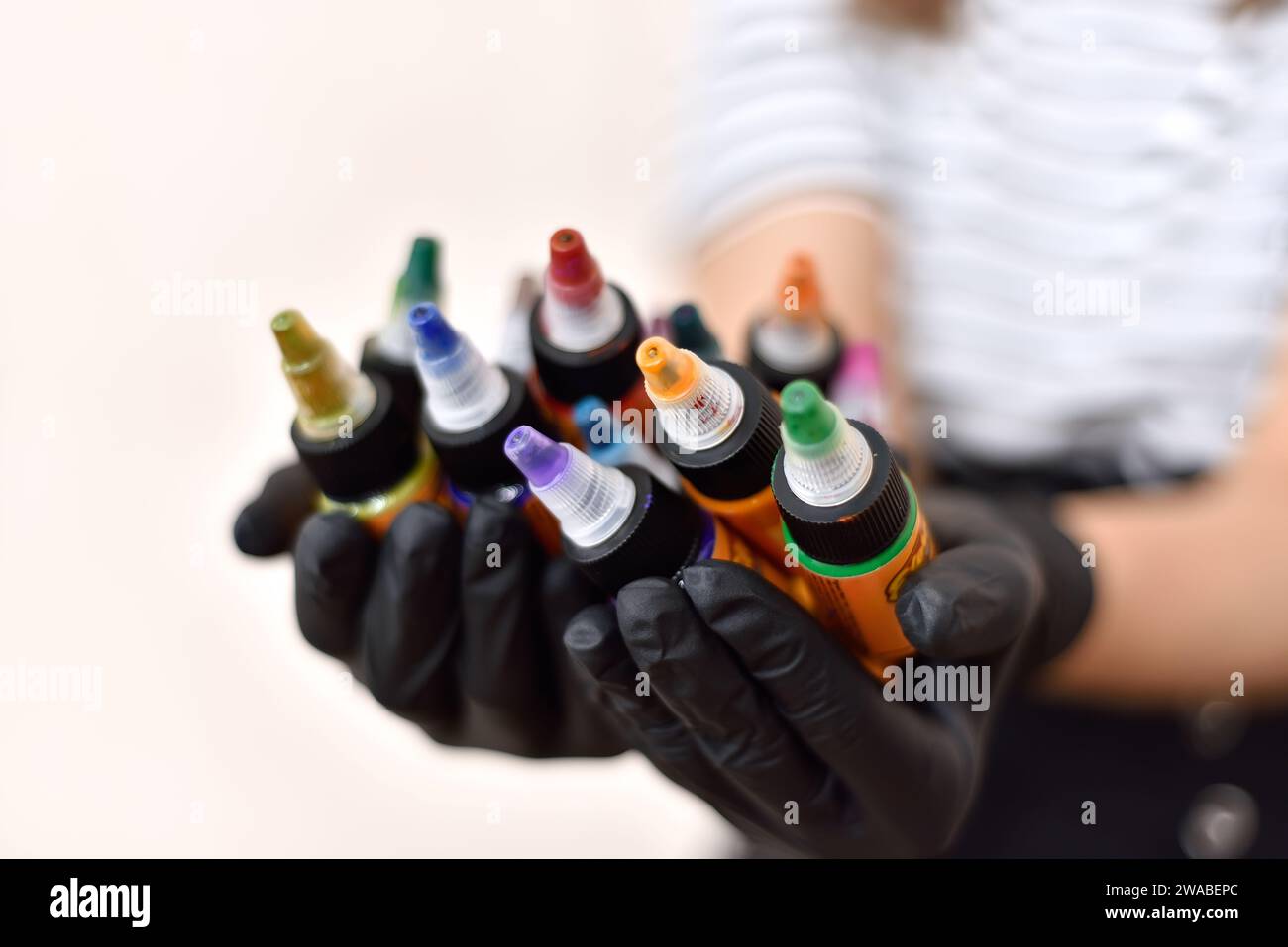 Frau, die sich tätowiert, hält Flaschen mit bunter Tattoo-Tinte. Kunst- und Designkonzept. Nahaufnahme Stockfoto