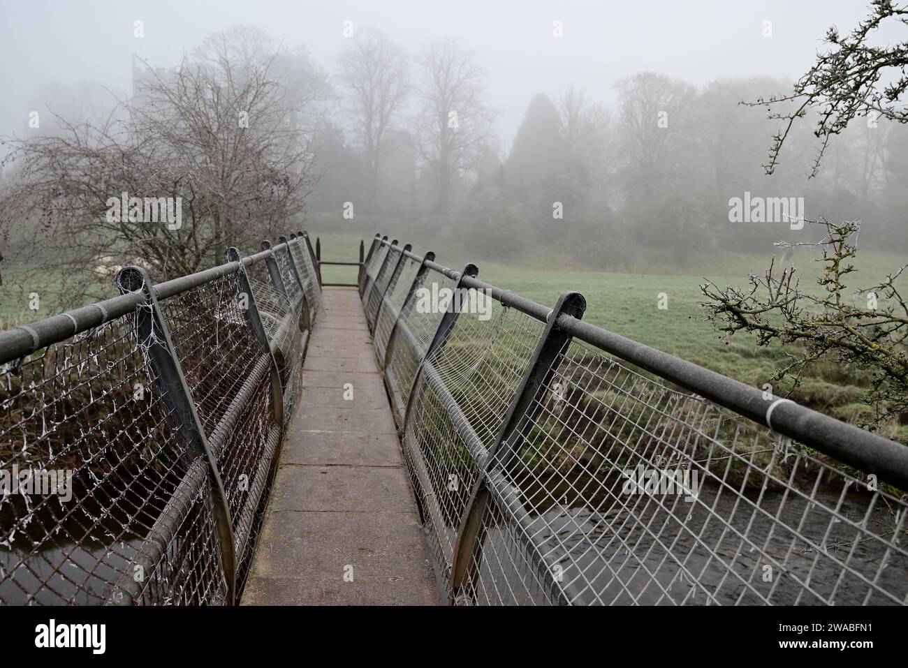 Eine Fußgängerbrücke über den Fluss Arrow in der Nähe von Studley an einem nebeligen Morgen im Winter. Stockfoto