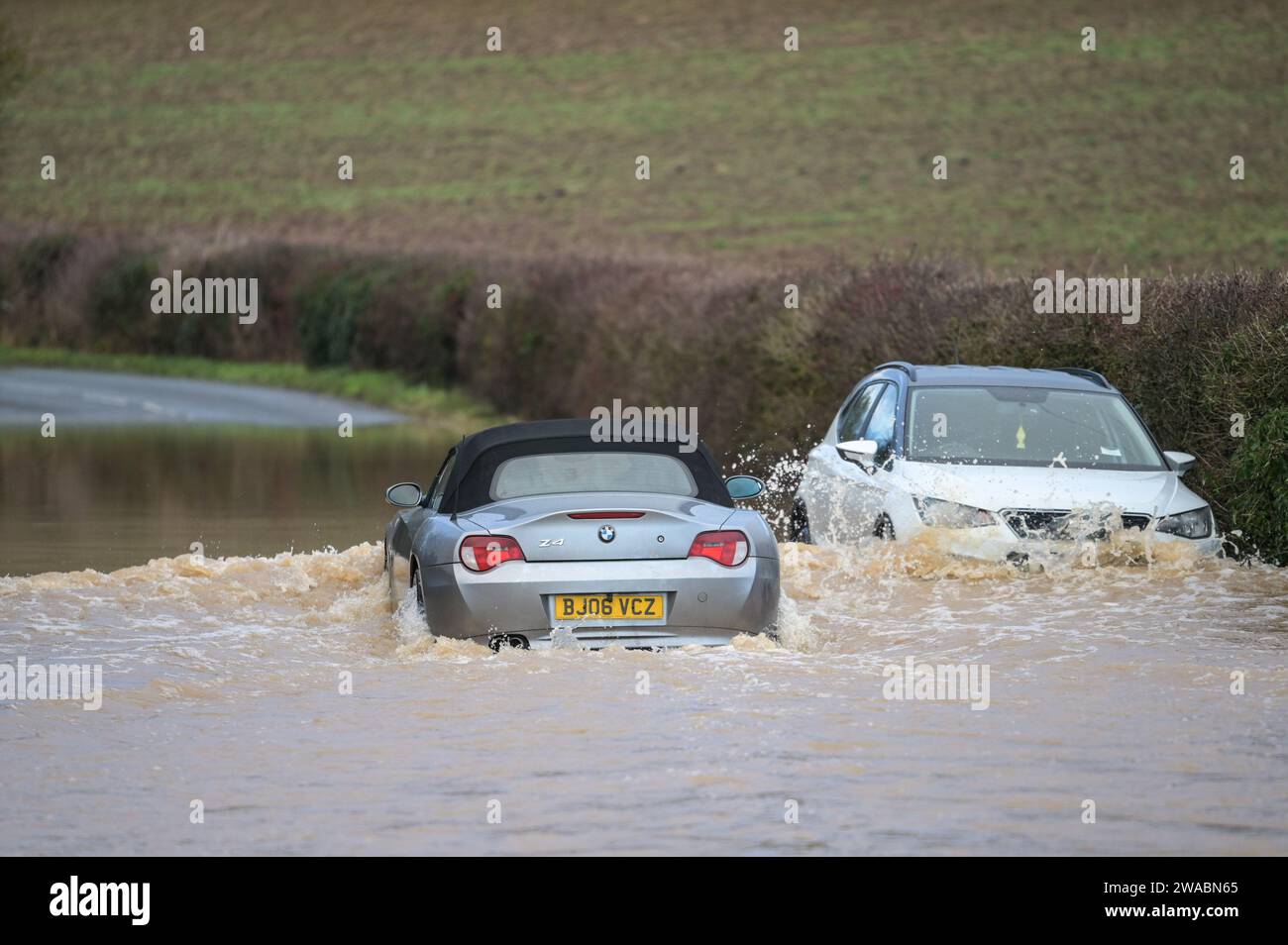 Offenham, Evesham, 3. Januar 2024 – Ein BMW-Fahrer versuchte und scheiterte, durch Hochwasser zu fahren, obwohl ein anderes Fahrzeug bereits auf derselben Strecke verlassen wurde. Der ältere Fahrer drehte seinen Motor auf, als er durchfuhr, aber seine Geschwindigkeit war zu hoch und Wasser stieg in seinen Motor ein. Das Fahrzeug ging schließlich wieder los, aber es kam nur wenige Meter vom Trockenland entfernt zu einer weiteren Haltestelle. Ein Straßenarbeiter kam dann an und legte als letzte Beleidigung ein Schild mit der Aufschrift „Road Closed“ vor sein Fahrzeug. Es geschah neben dem Offenham Caravan Park, der sich in der Nähe von Evesham in Worcestershire befindet, wo der Fluss Avon niederfließt Stockfoto