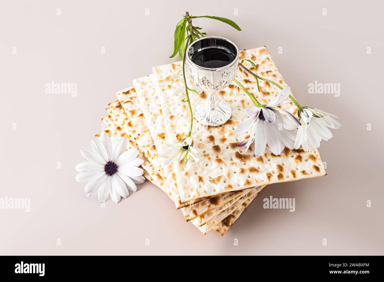 Das Konzept des Judenfestes am Pessach. Ein Stapel Matza und eine silberne Tasse mit Rotwein und einer zarten Blume. Pastellhintergrund Stockfoto