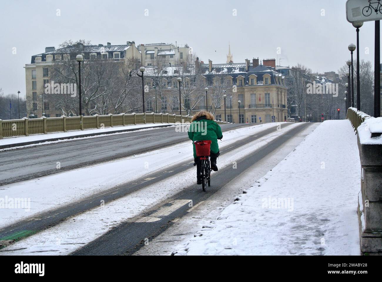 Unerwarteter Schnee in Paris. Eine einsame Frau fährt mit dem Fahrrad entlang der verlassenen Alma-Brücke. Stockfoto