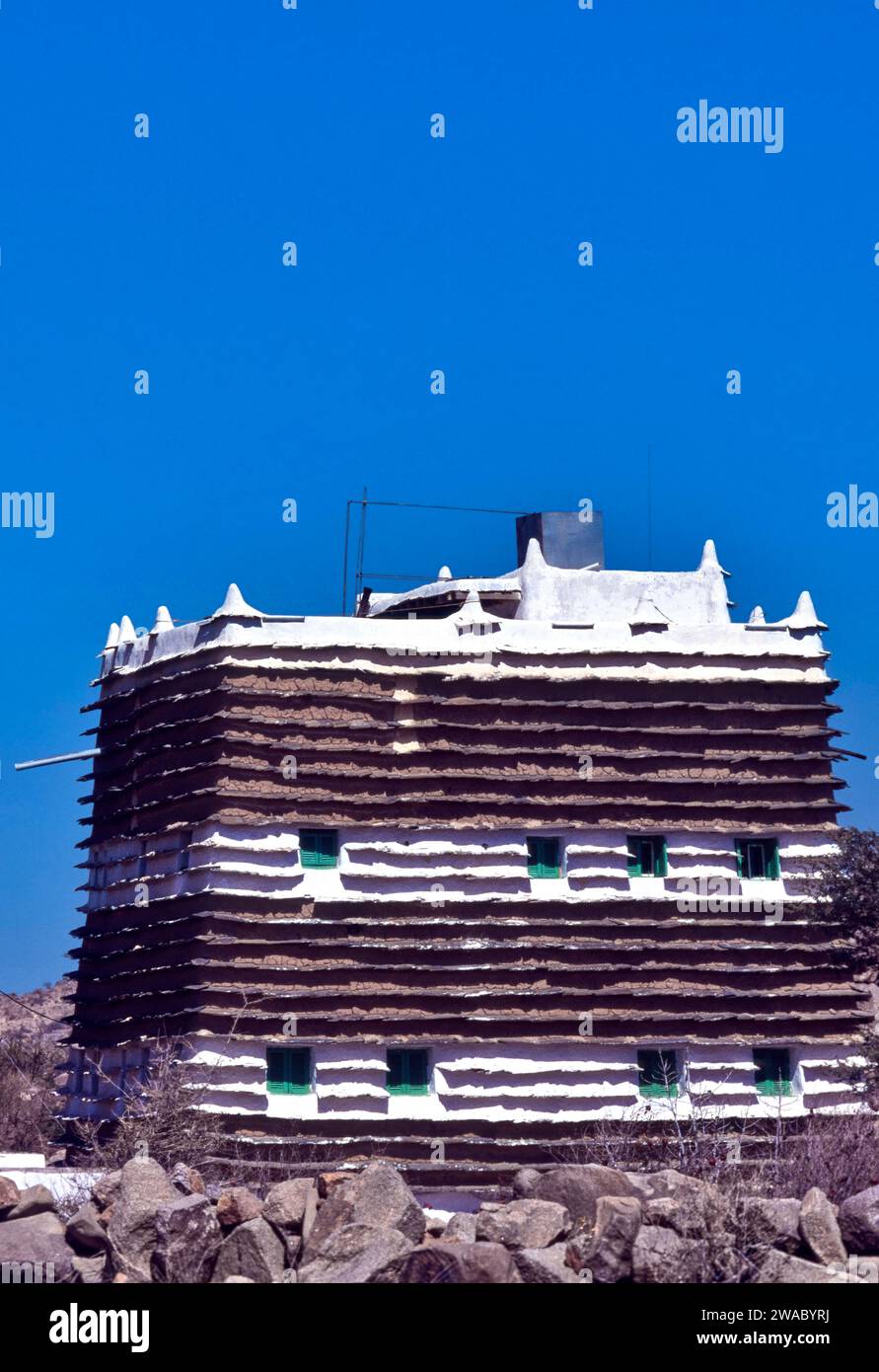 Saudiarabischer blauer Himmel über einem typischen alten, schlammigen Dorfhaus mit kleinen Fenstern und grünen Fensterläden Stockfoto