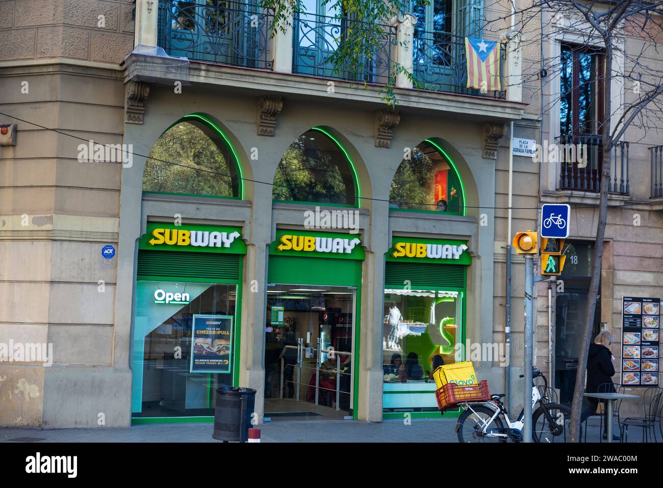 Barcelona, Spanien - 30. November 2023: U-Bahn-Restaurant mit einem Glovo-Lieferrad in einer Einkaufsstraße von Barcelona, Katalonien, Spanien Stockfoto