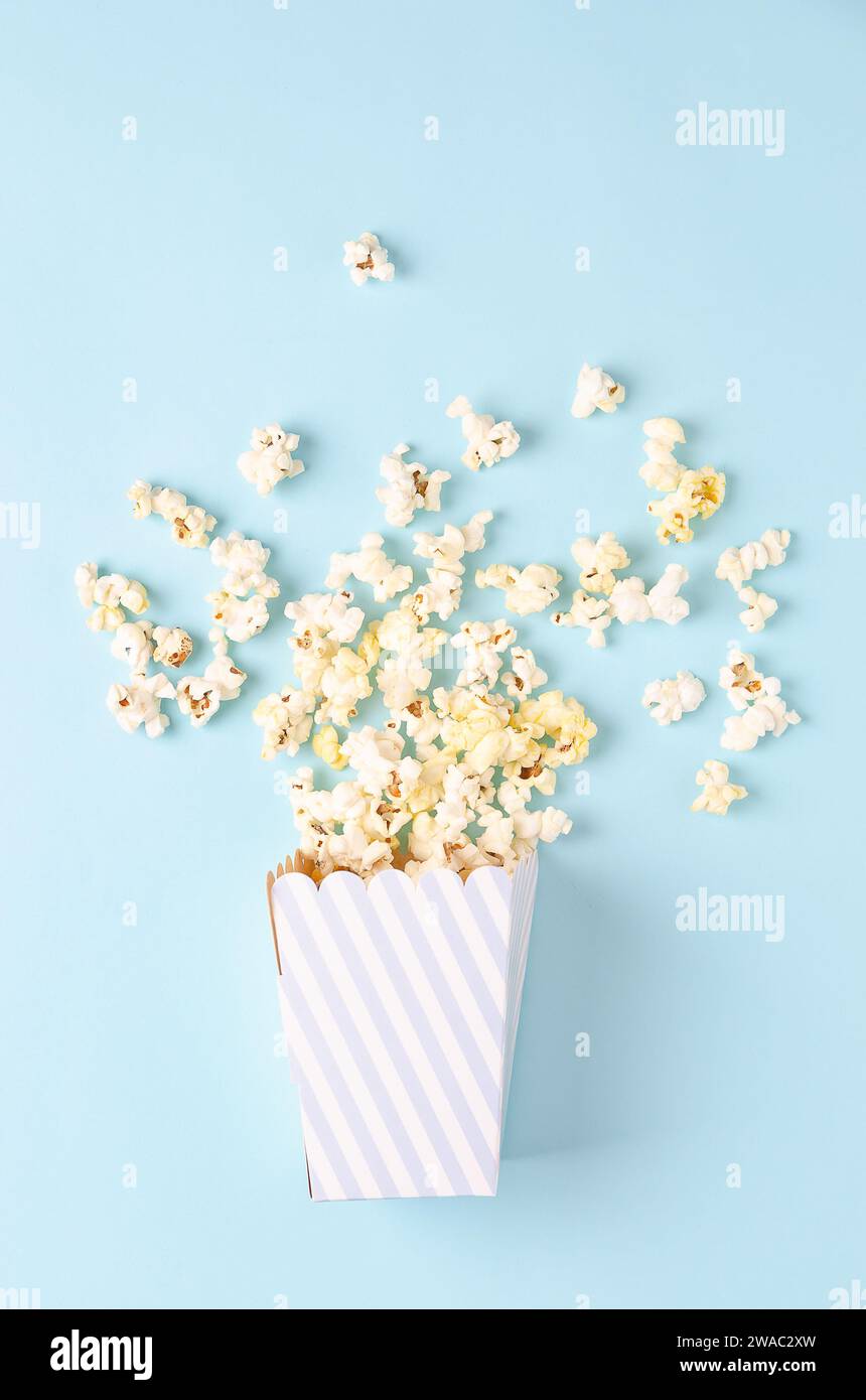 Ein gestreifter Eimer Popcorn auf hellblauem Hintergrund, Draufsicht und Kopierraum. Vertikales Format. Stockfoto