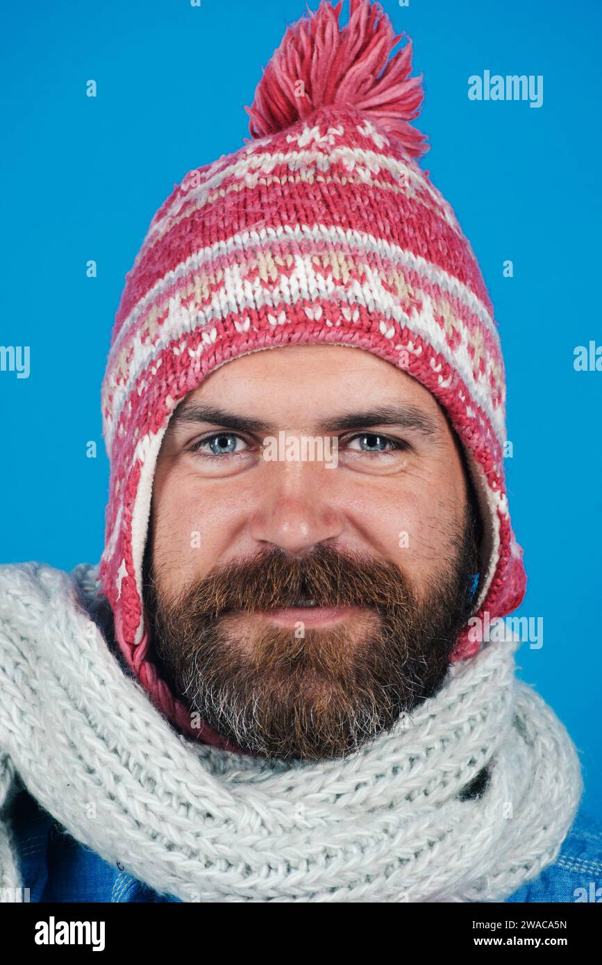 Wintermode für Herren. Nahaufnahme Porträt eines lächelnden Mannes in gestricktem Schal und Hut. Modische Accessoires für den Winter. Hübscher trendiger Mann mit Wintermütze und Stockfoto